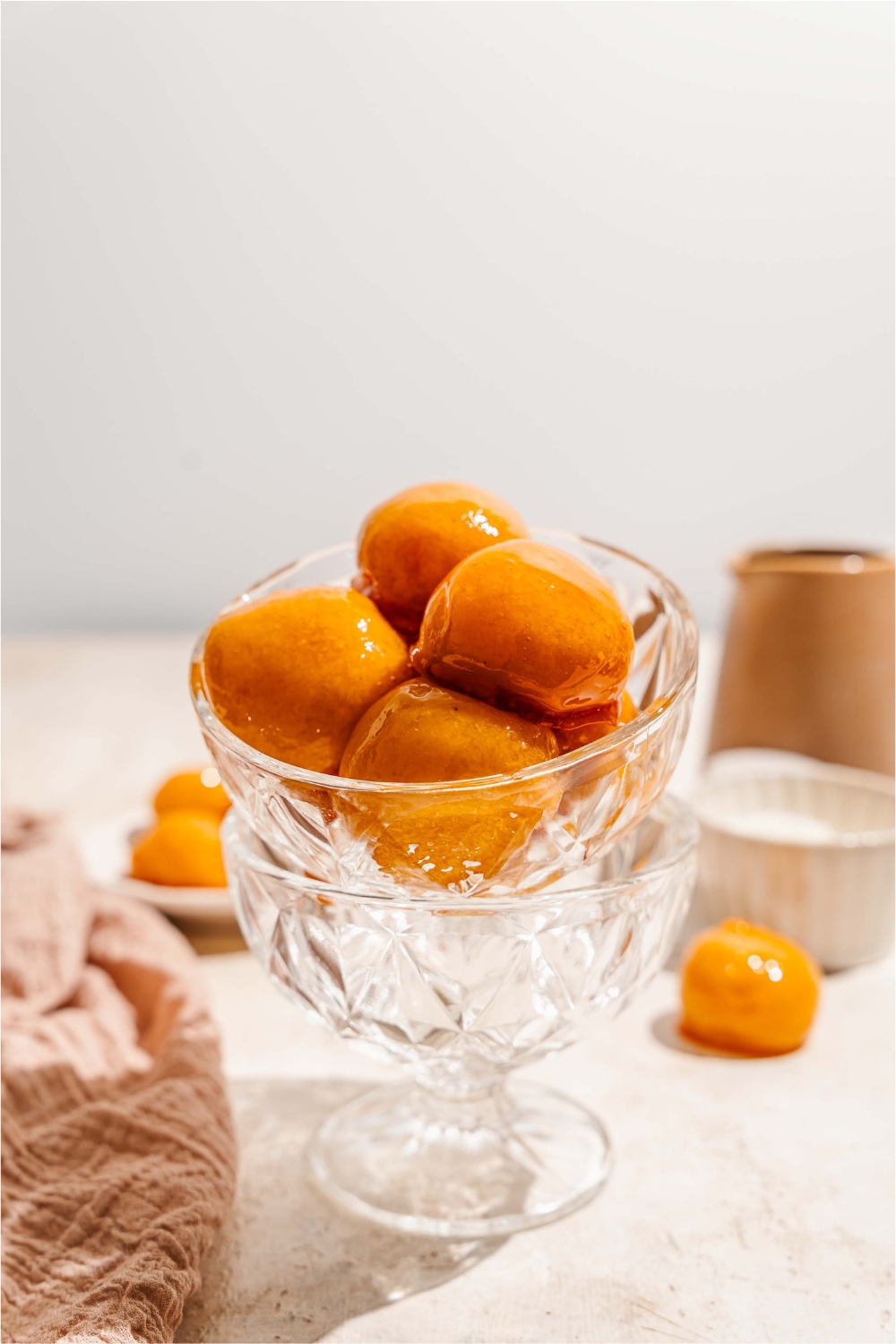 A glass bowl with several pieces of bala baiana balls stacked in another glass bowl. The bowl is on a tan counter with an additional bowl of bala baiana.