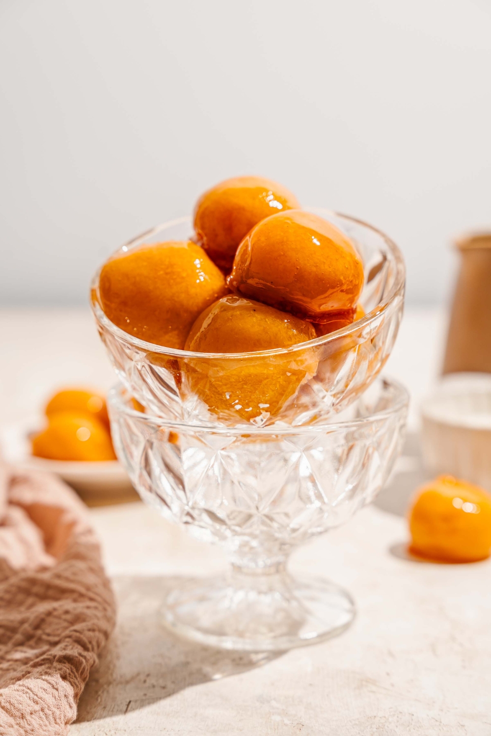 A glass bowl with several pieces of bala baiana balls stacked in another glass bowl. The bowl is on a tan counter with an additional bowl of bala baiana.