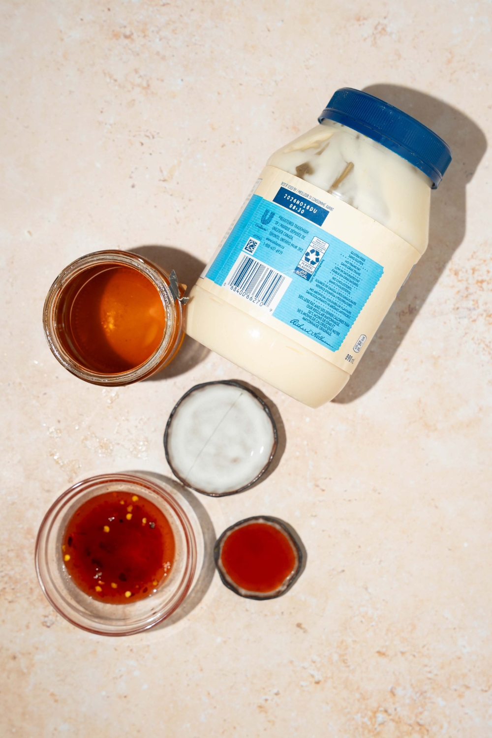 A tan counter with ingredients to make bang bang sauce including mayo, sweet chili sauce, Tabasco sauce, honey, and vinegar.