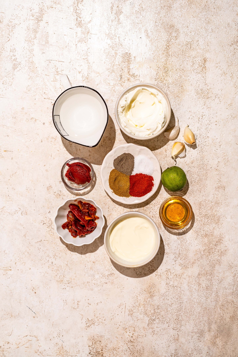 A tan counter with several bowls containing ingredients to make burrito sauce including greek yogurt, sour cream, chipotle peppers, tomato paste, lime, and spices.