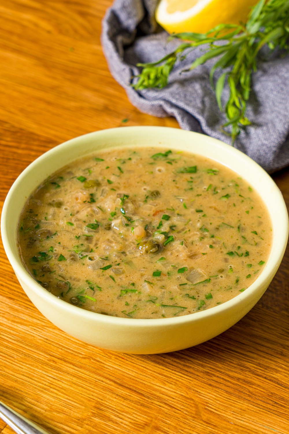 A bowl of chicken piccata sauce. The bowl is on a wooden counter.