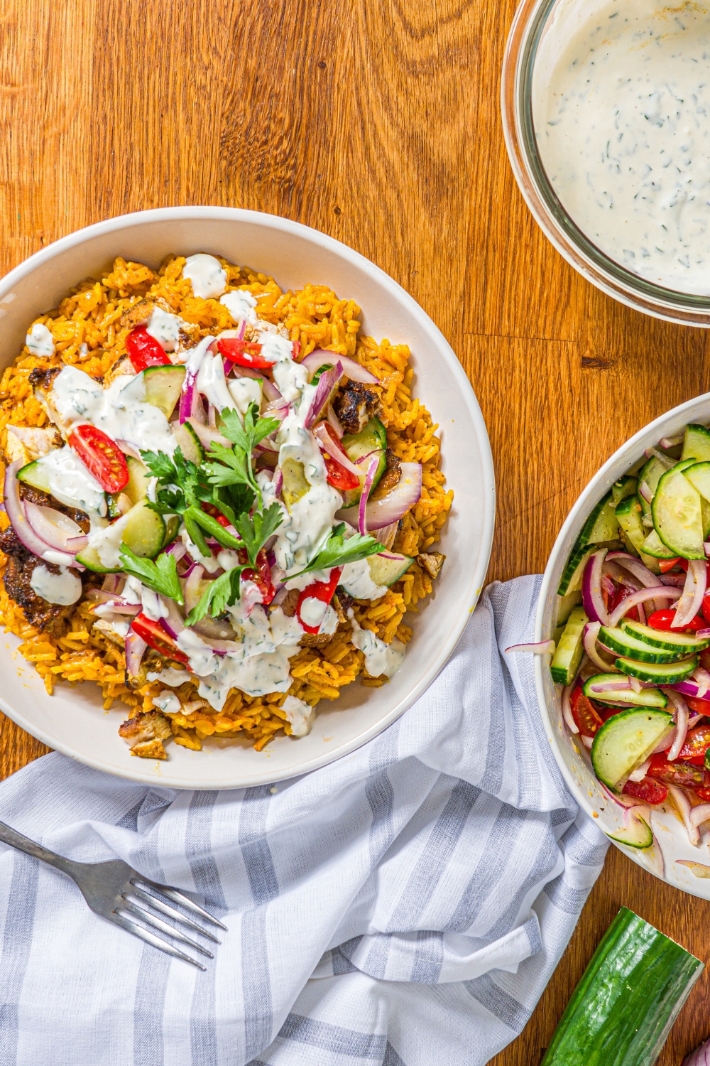 A white bowl with chicken shawarma bowl served with seasoned rice, chicken shawarma, onion salad, and garlic sauce garnished with fresh parsley. The bowl is on a wooden counter with a bowl of onion salad and bowl of garlic sauce.