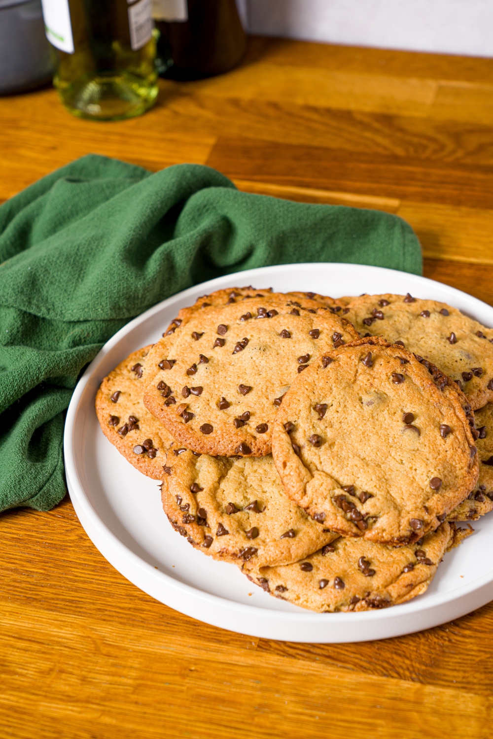 A white plate with chocolate chip cookies without baking soda. The plate is on a wooden counter with a green cloth napkin.