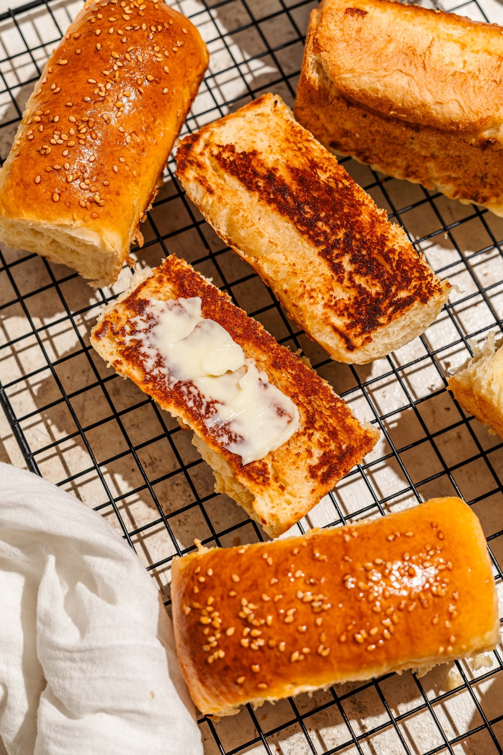 A wire rack with several pieces of Raising Cane's bread. One of the pieces is sliced in half and toasted with butter.