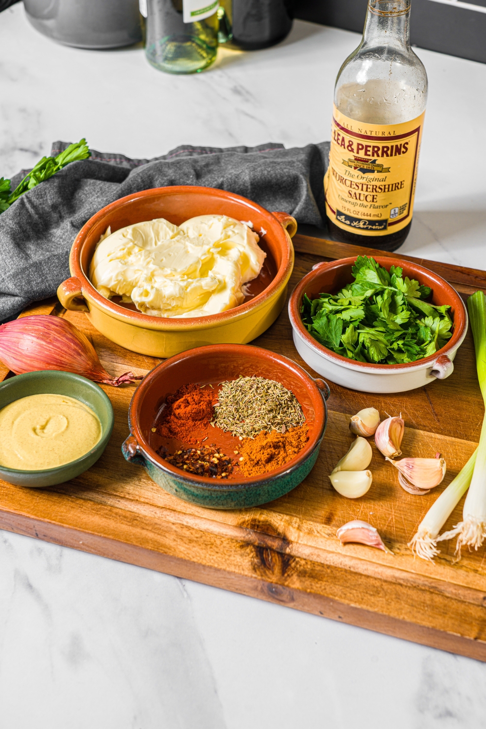 A wooden board with ingredients to make cowboy butter including butter, mustard, garlic, green onion, red onion, fresh parsley, worcestershire sauce, and seasonings.