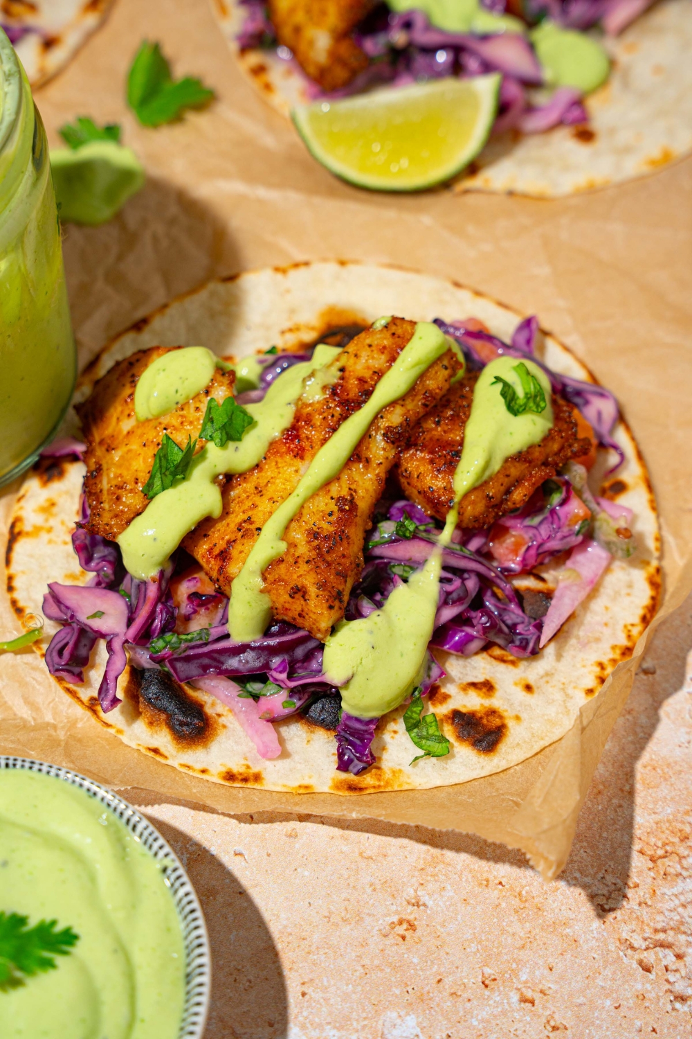 A tan counter with parchment paper and several open fish tacos. The tacos are served with cabbage and drizzled with fish taco sauce.