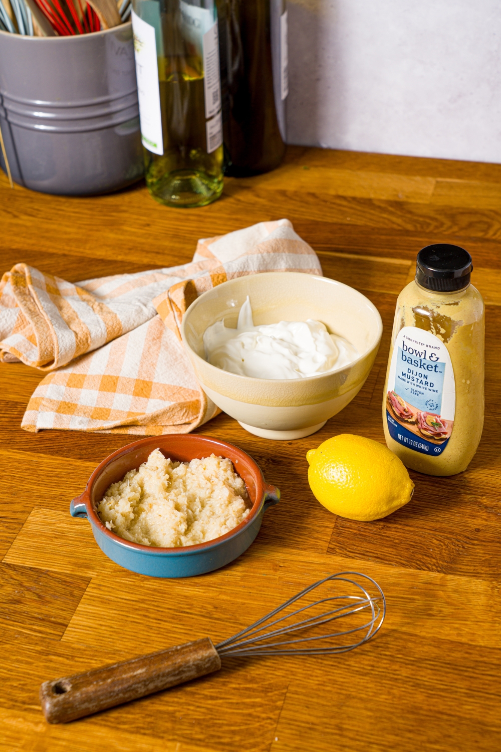 A wooden counter with ingredients to make horseradish sauce including sour cream, horseradish, lemon, and mustard.