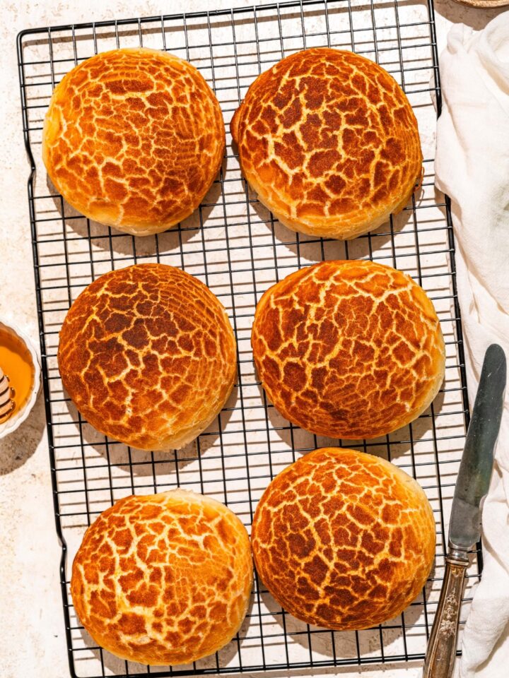 A wire rack with baked Dutch Crunch bread loaves. The rack is on a tan counter with a knife.