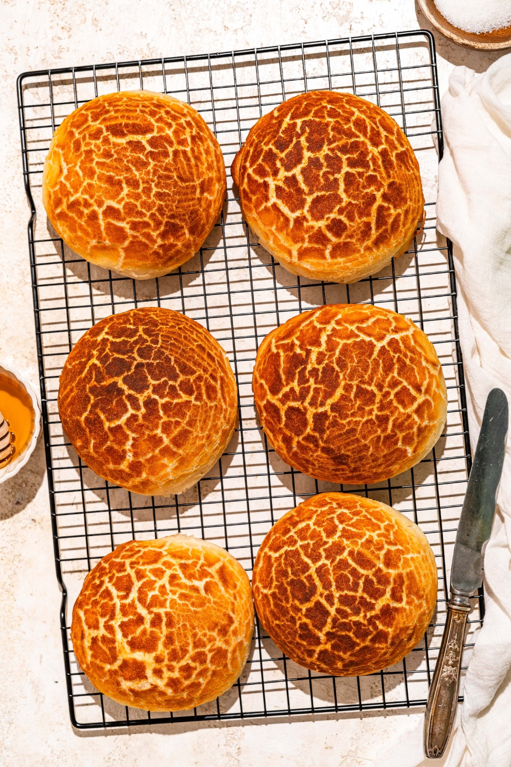 A wire rack with baked Dutch Crunch bread loaves. The rack is on a tan counter with a knife.