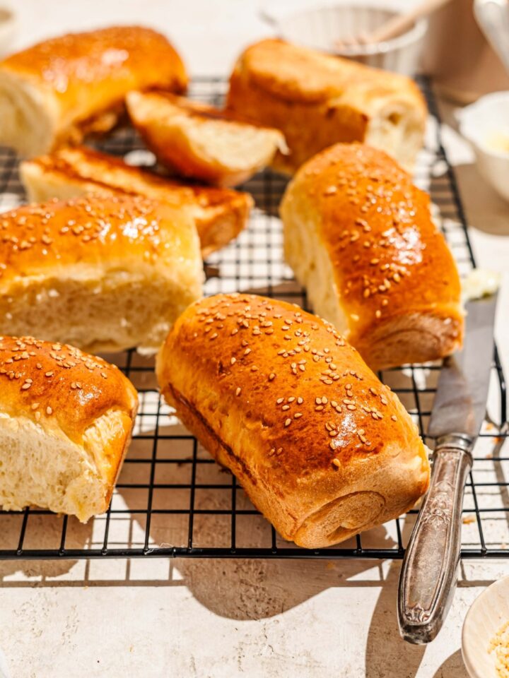 A wire rack with several pieces of Raising Cane's bread topped with sesame seeds. The rack is on a tan counter with a buttered knife.