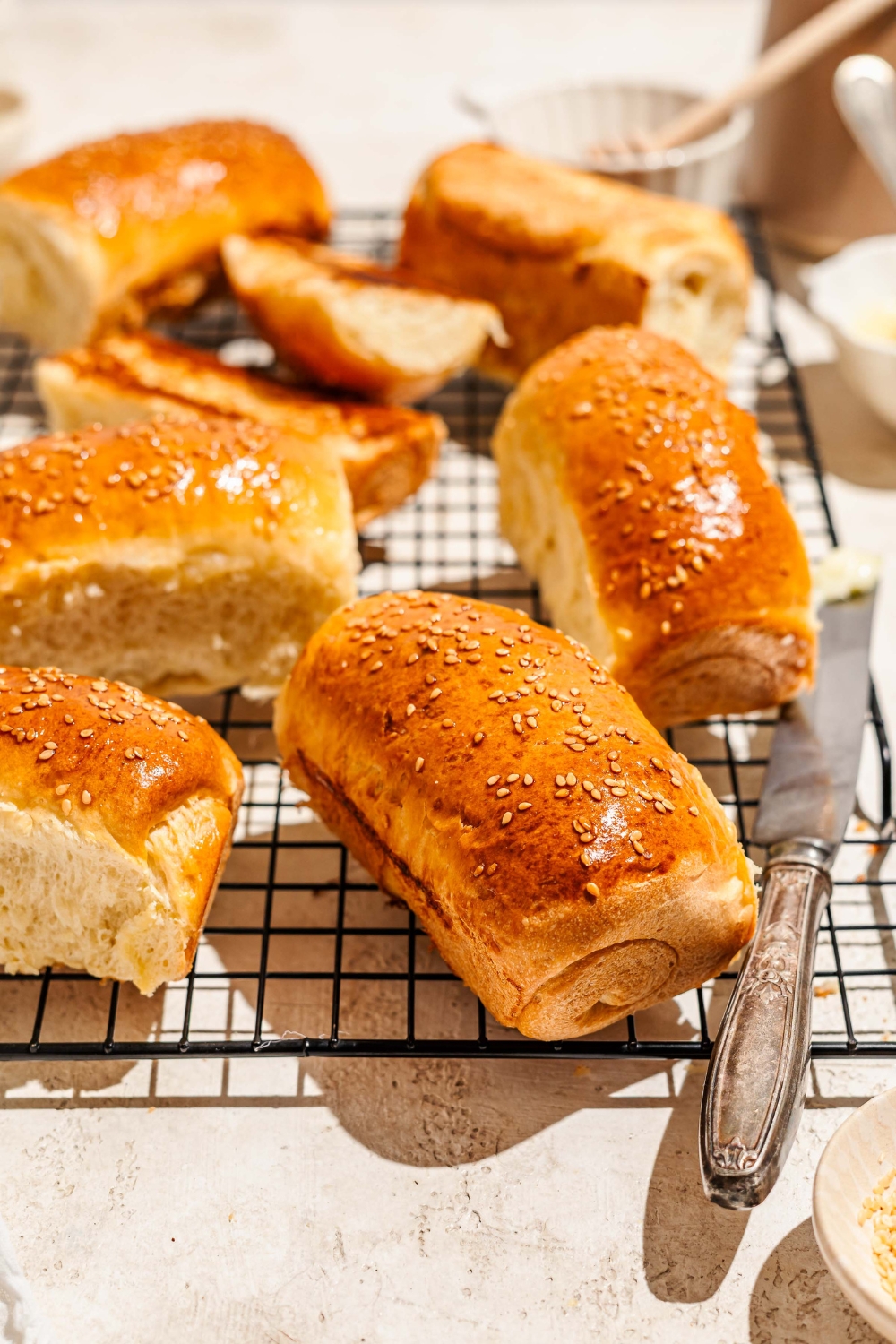 A wire rack with several pieces of Raising Cane's bread topped with sesame seeds. The rack is on a tan counter with a buttered knife.