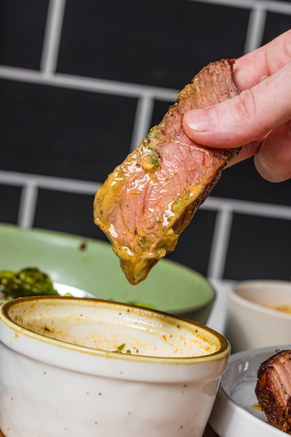 A close up of a hand dipping a steak into a bowl of cowboy butter.