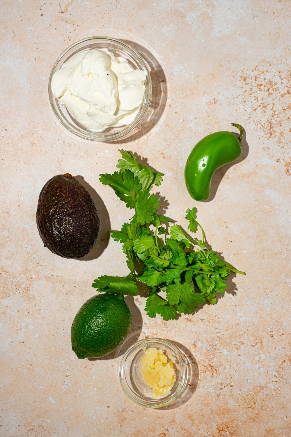 A tan counter with ingredients to make fish taco sauce including sour cream, cilantro, avocado, lime, and jalapeño/