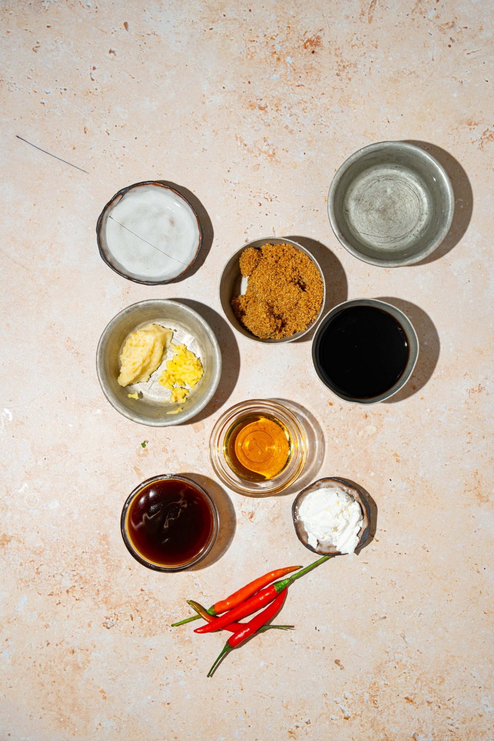 A tan counter with several bowls containing ingredients to make general tso sauce including brown sugar, hoisin, ginger, garlic, water, red chiles, rice vinegar, and soy sauce.