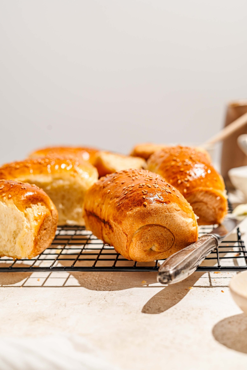A wire rack with several pieces of Raising Cane's bread topped with sesame seeds. The rack is on a tan counter with a buttered knife.