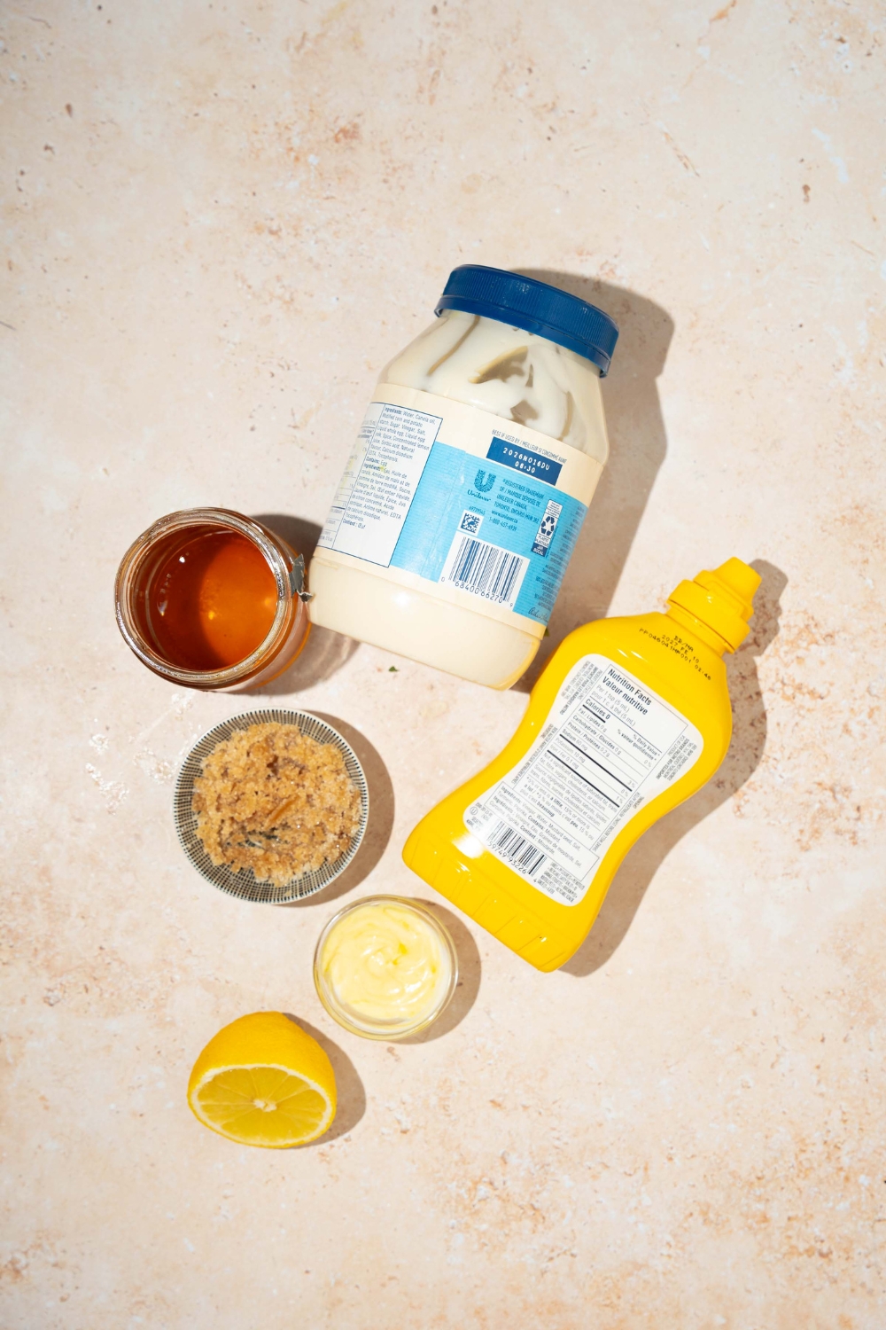 A tan counter with ingredients to make honey mustard sauce including honey, yellow mustard, dijon mustard, brown sugar, lemon, and mayo.