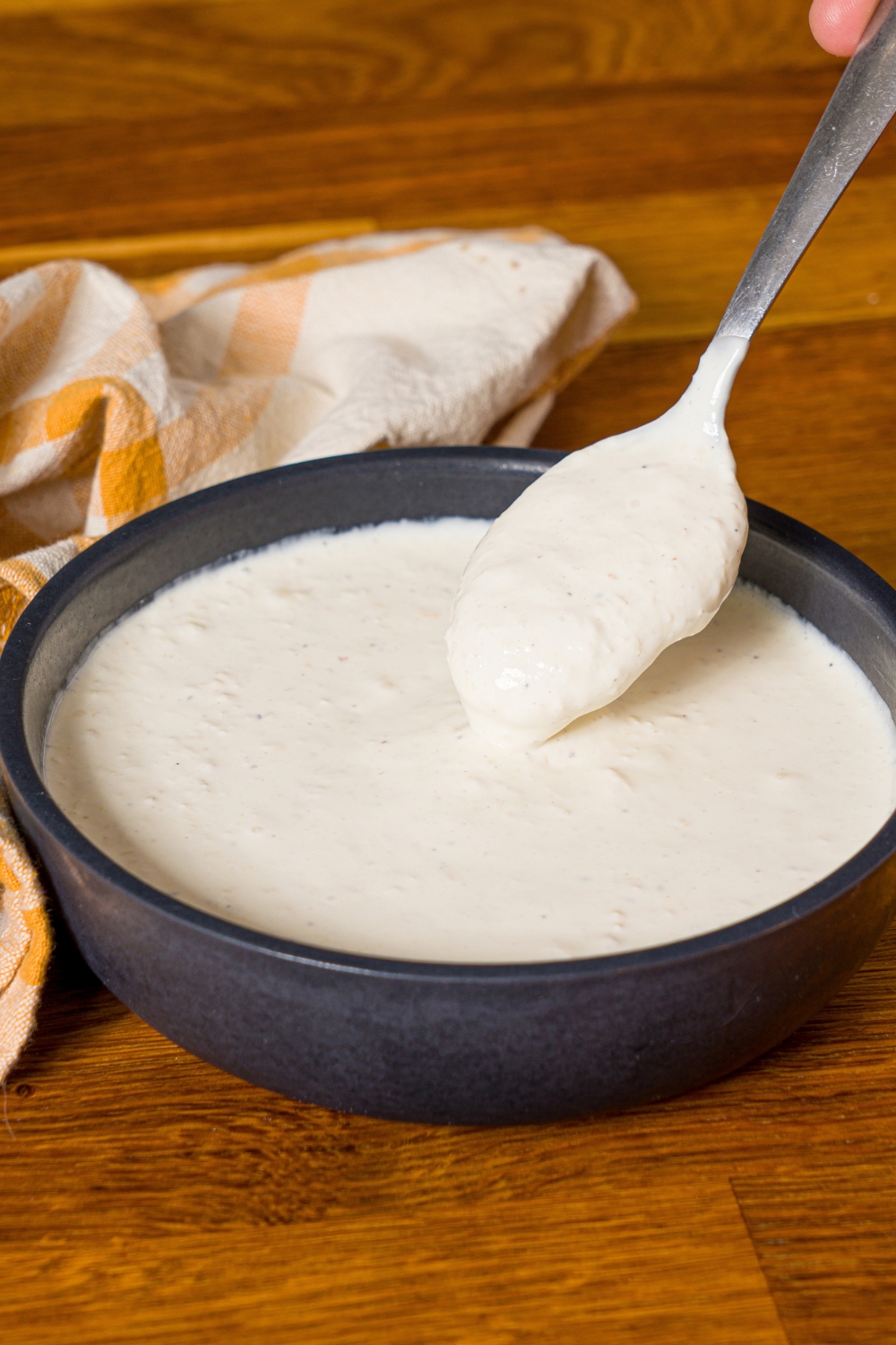 A bowl of horseradish sauce with a spoon dipping in the bowl. The bowl is on a wooden counter with a yellow checkered napkin.