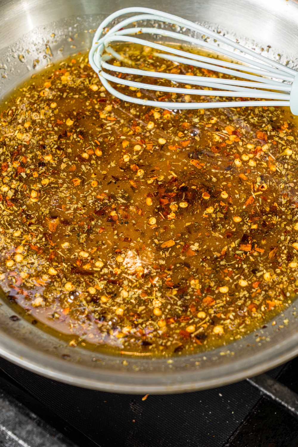 A skillet with a whisk mixing sweet chili sauce including maple syrup, red chili flakes, butter, and seasonings.