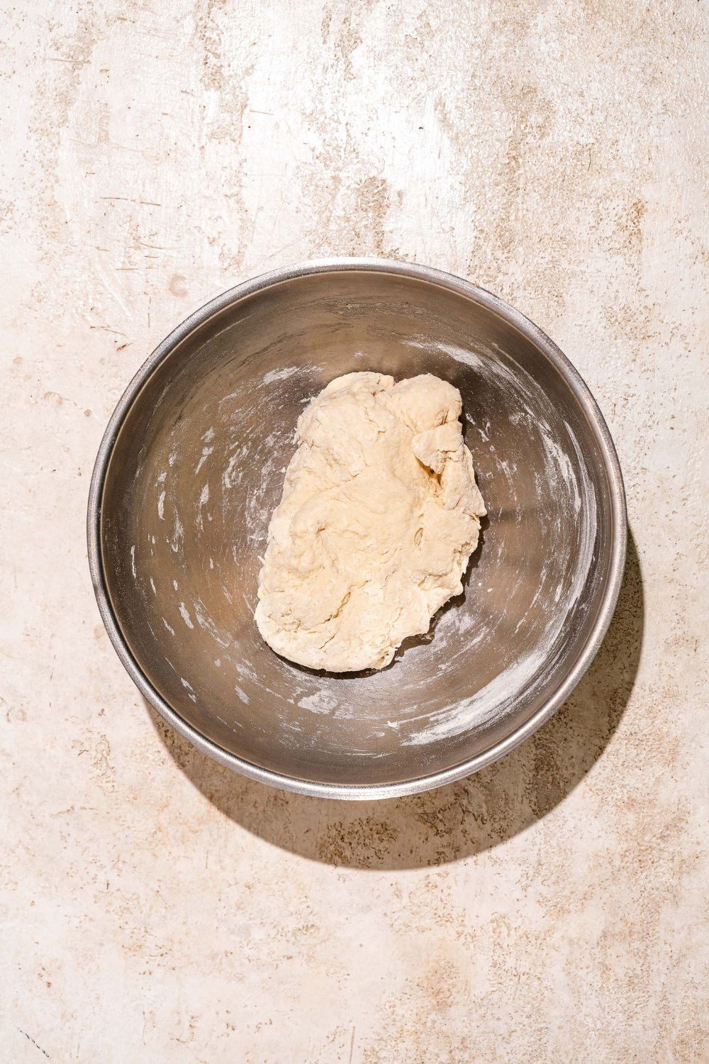 A large bowl with a shaggy dough mixture to make Dutch Crunch bread. The bowl is on a tan counter.