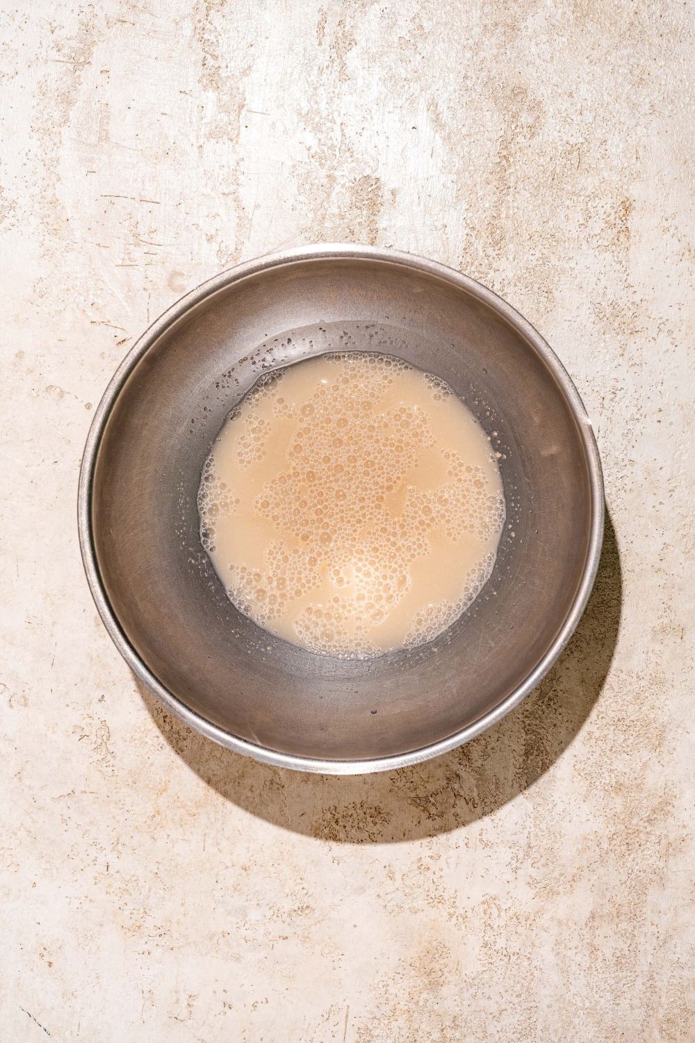 A large bowl with active yeast mixed with water. The bowl is on a tan counter.