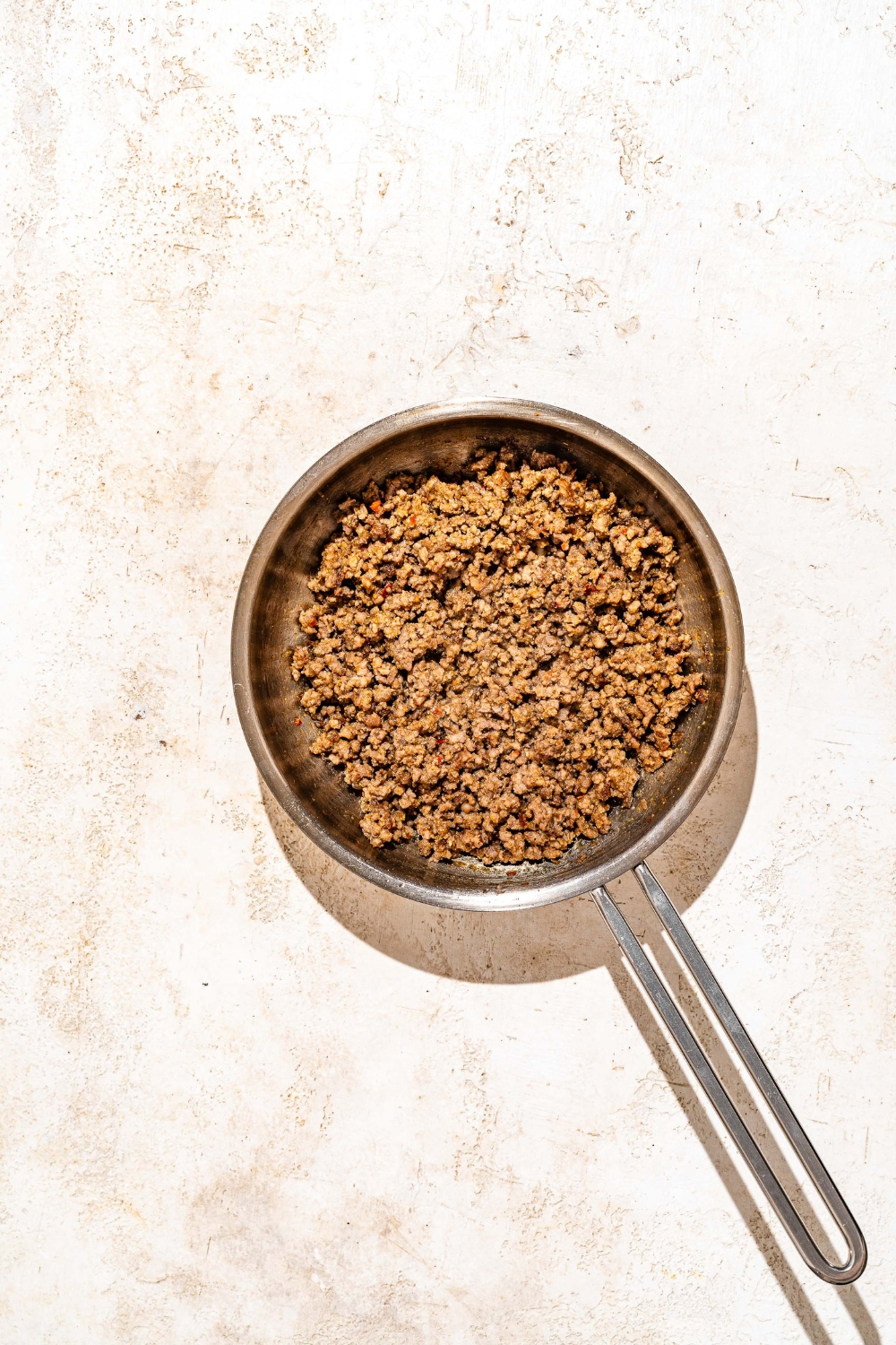 A skillet with cooked seasoned ground beef. The skillet is on a tan counter.