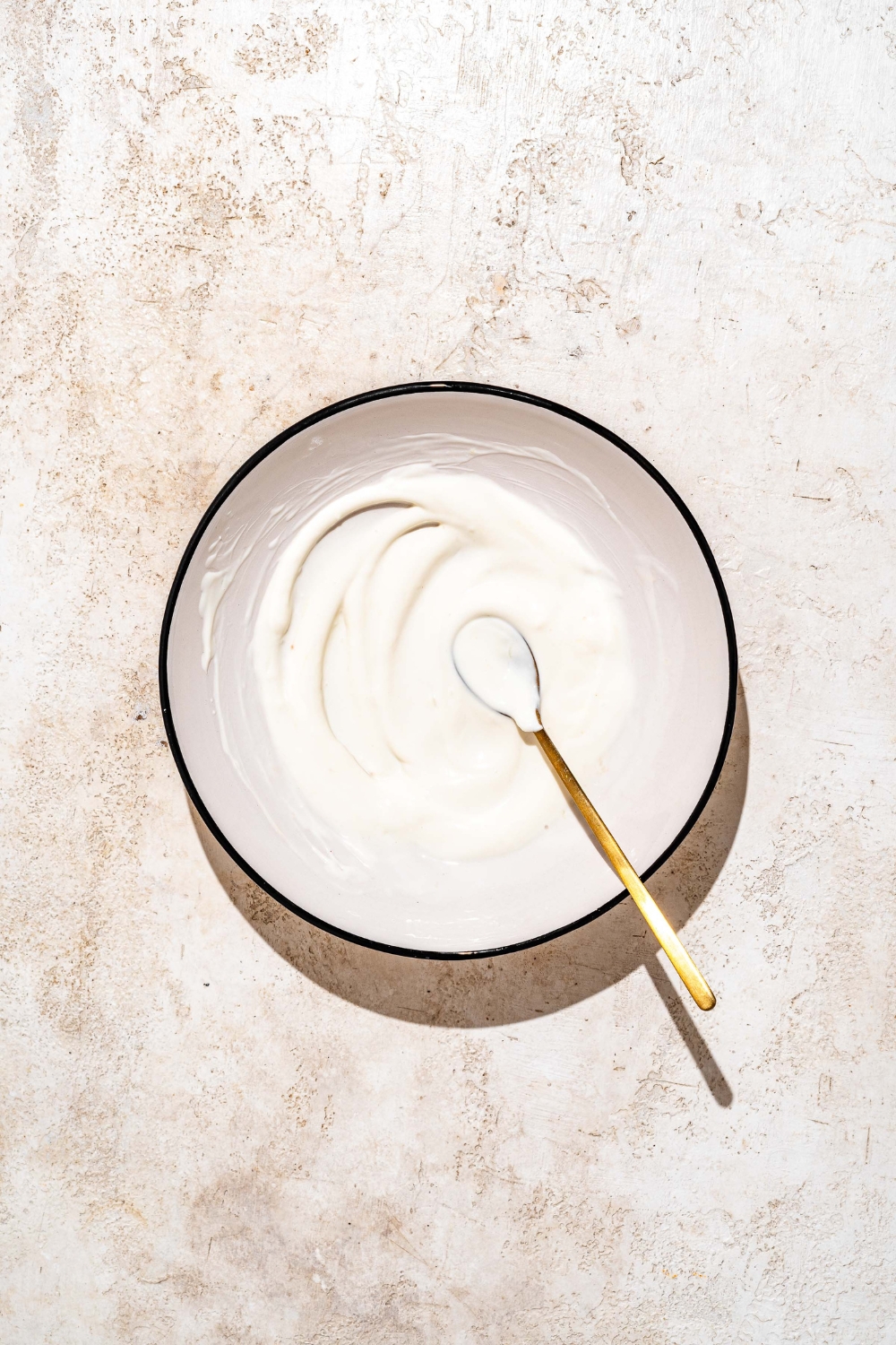 A bowl with a spoon mixing white sauce for tacos. The bowl is on a tan counter.