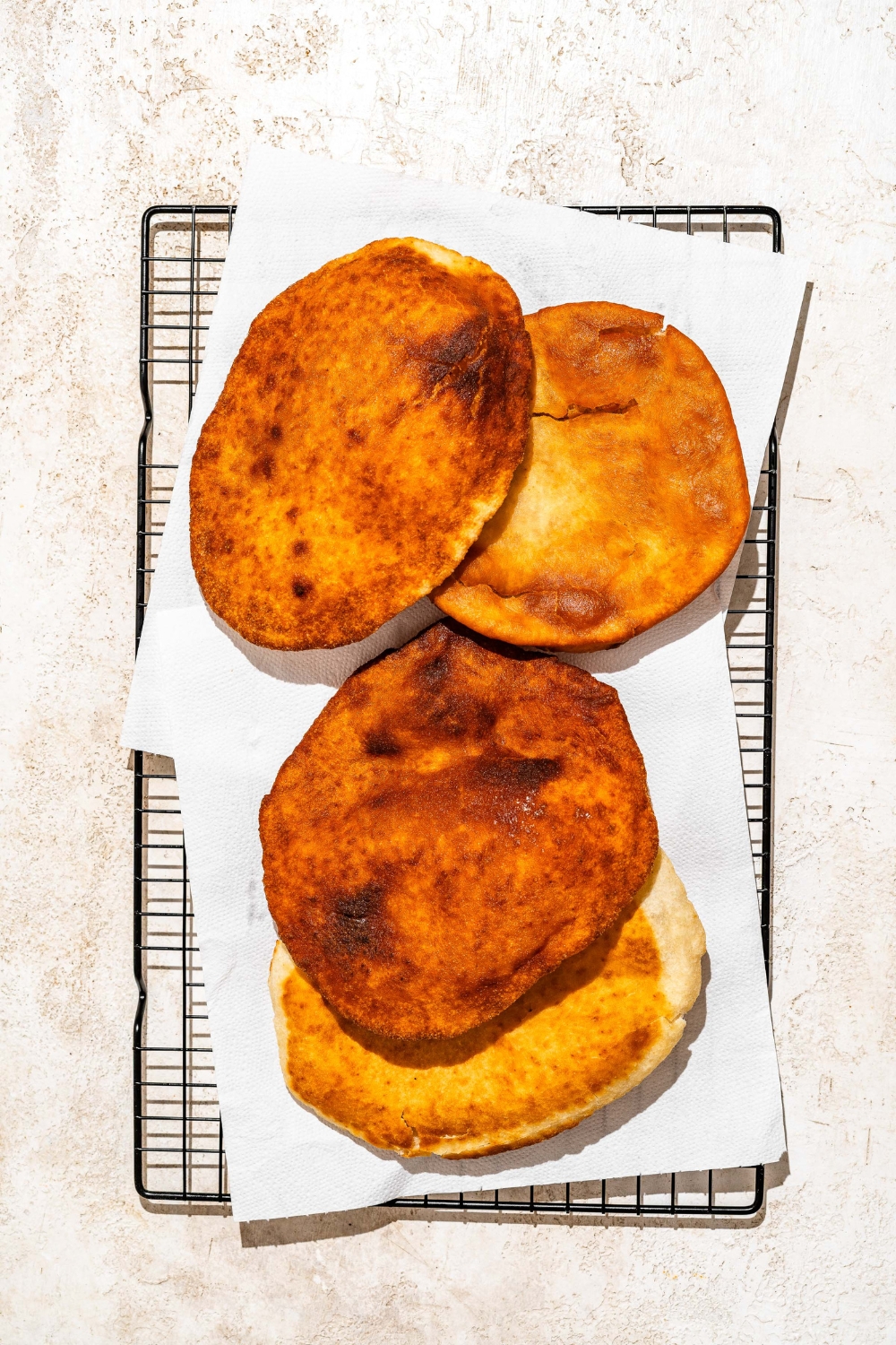 A drying rack lined with paper towels with several pieces of Indian fry bread. The rack is on a tan counter.