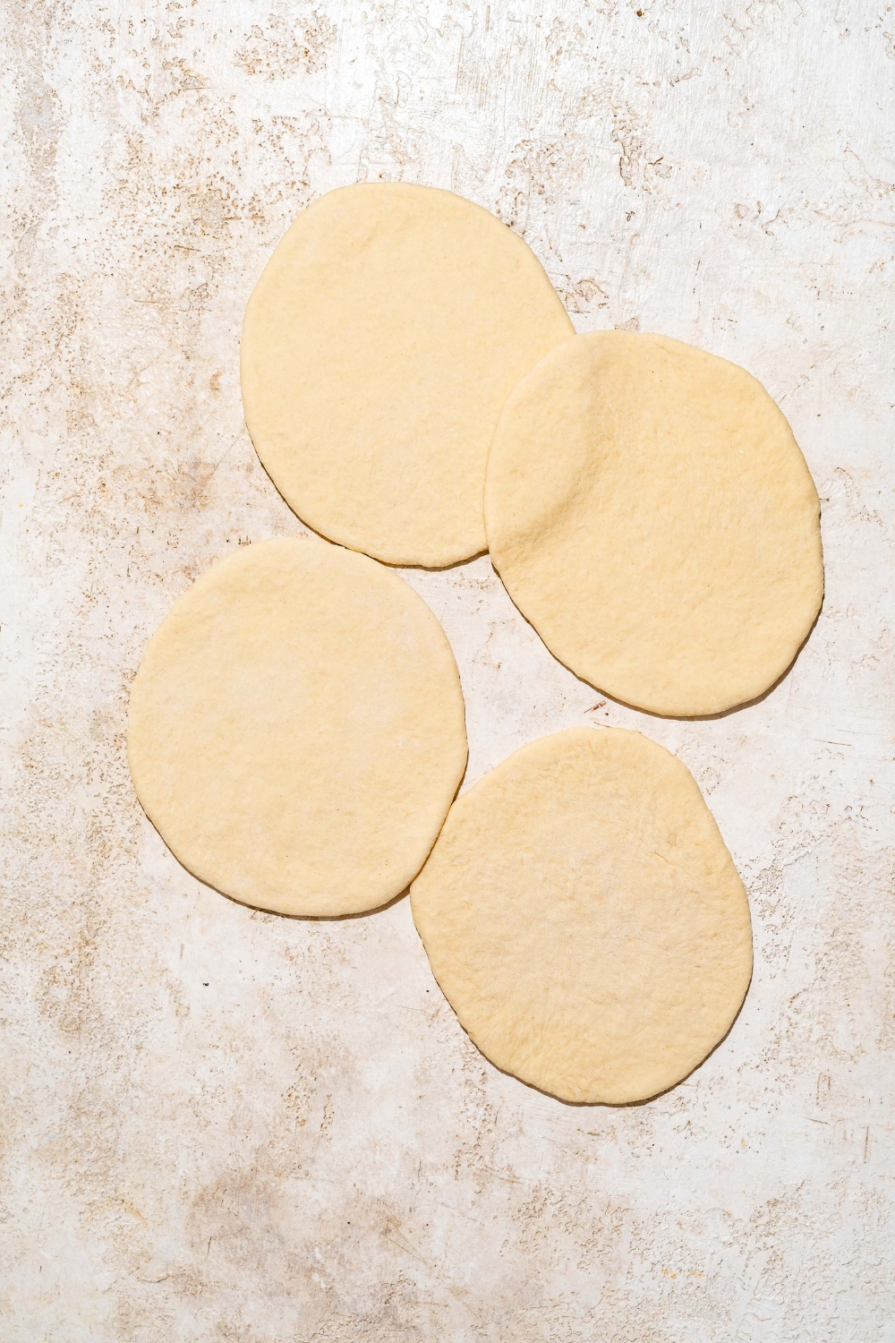Four shaped Indian fry bread dough. The dough is on a tan counter.