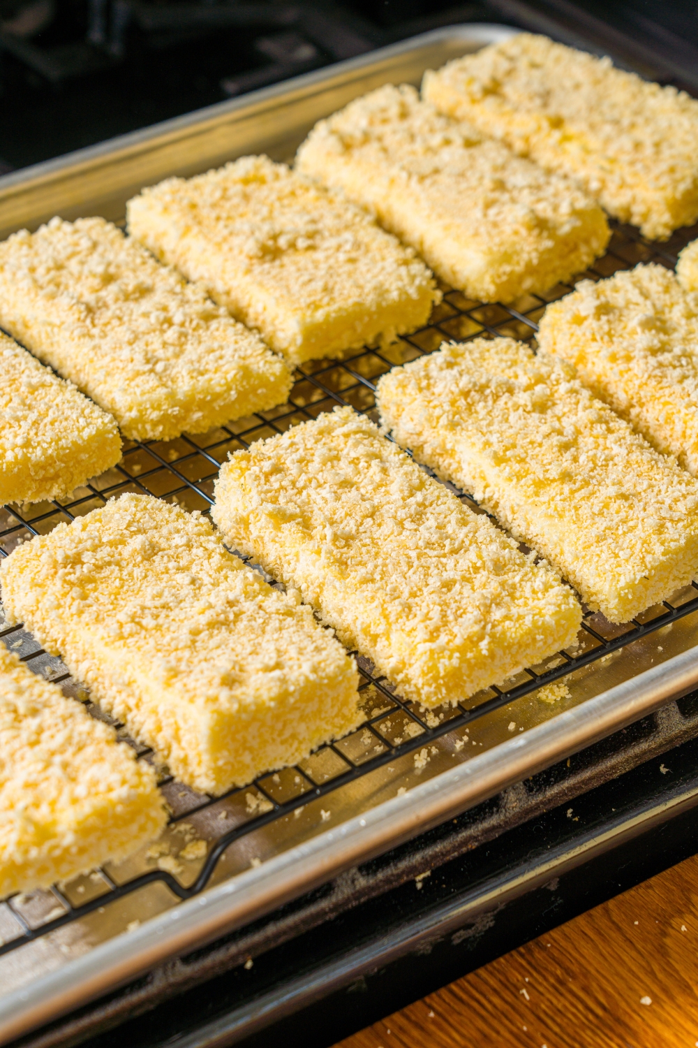 A baking sheet lined with a wire rack with breaded mozzarella sticks.