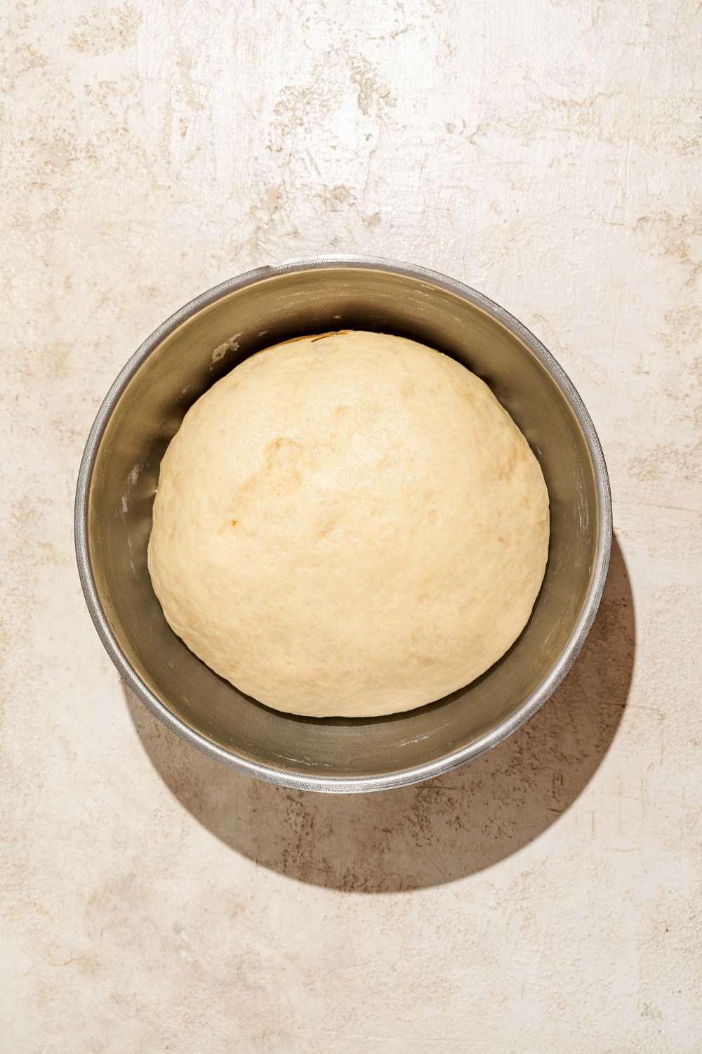 A large bowl with a proofed Raising Cane's bread dough ball. The bowl is on a tan counter.