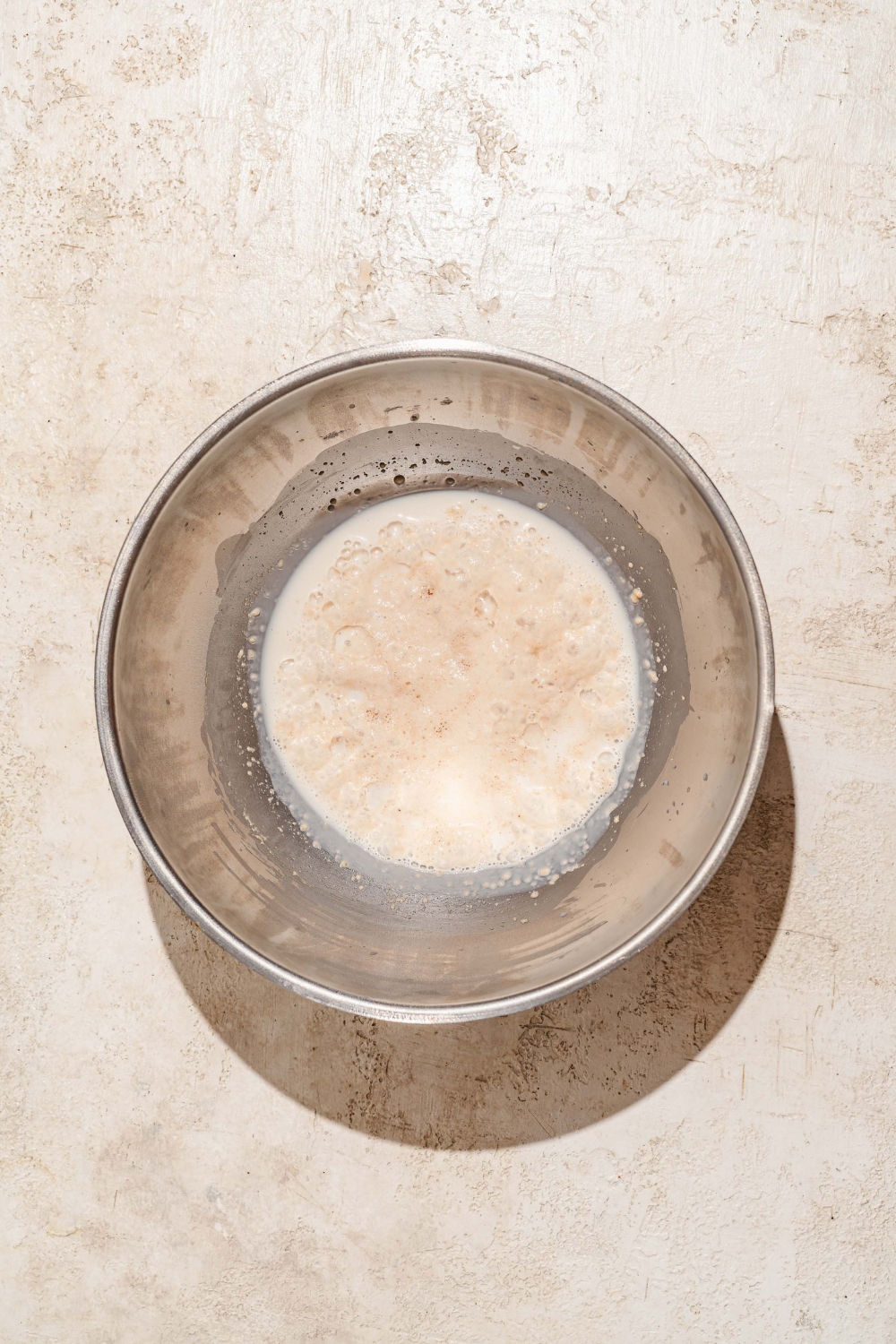 A large bowl with a yeast mixture. The bowl is on a tan counter.
