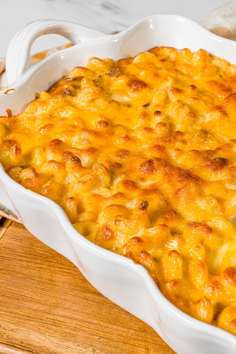A baking dish with baked bacon macaroni and cheese. The dish is on a wooden board.