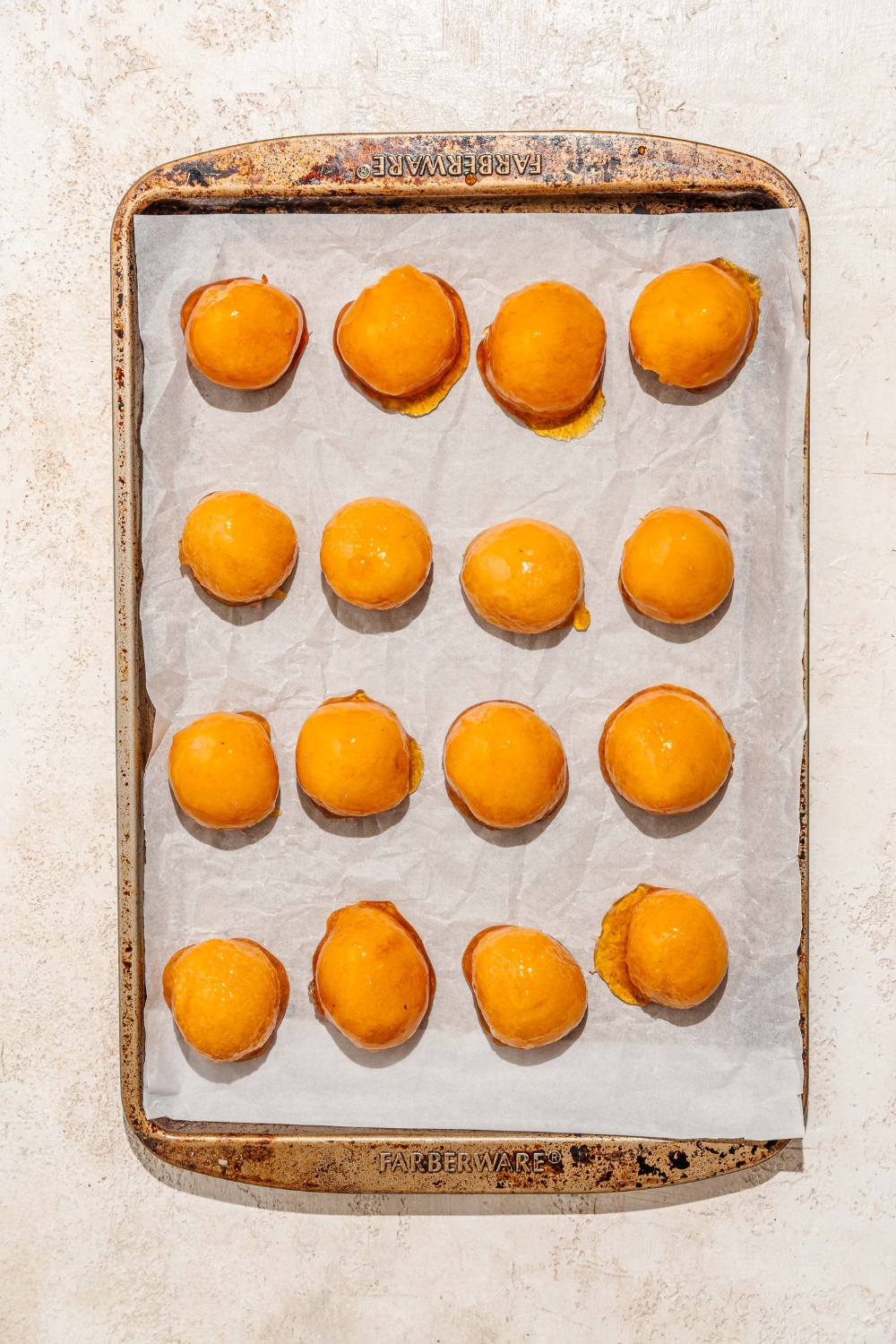 A baking sheet lined with parchment paper with several bala baiana balls dipped in caramel. The baking sheet is on a tan counter.