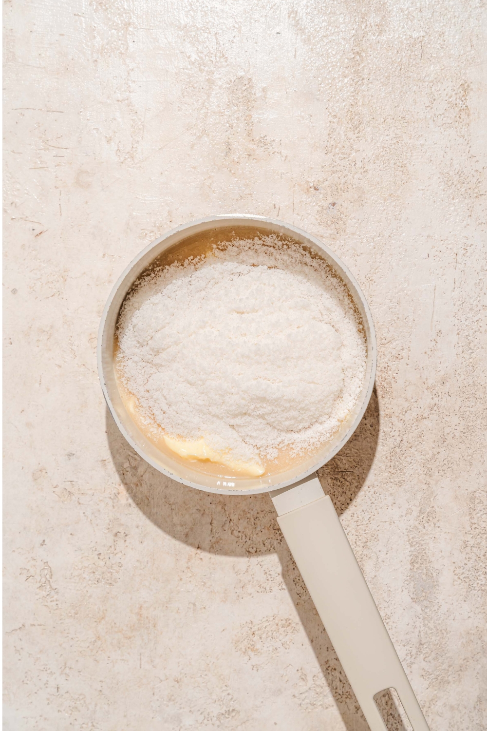 A saucepan with ingredients to make bala baiana dough including butter, shredded coconut, and condensed milk. The saucepan is on a tan counter.