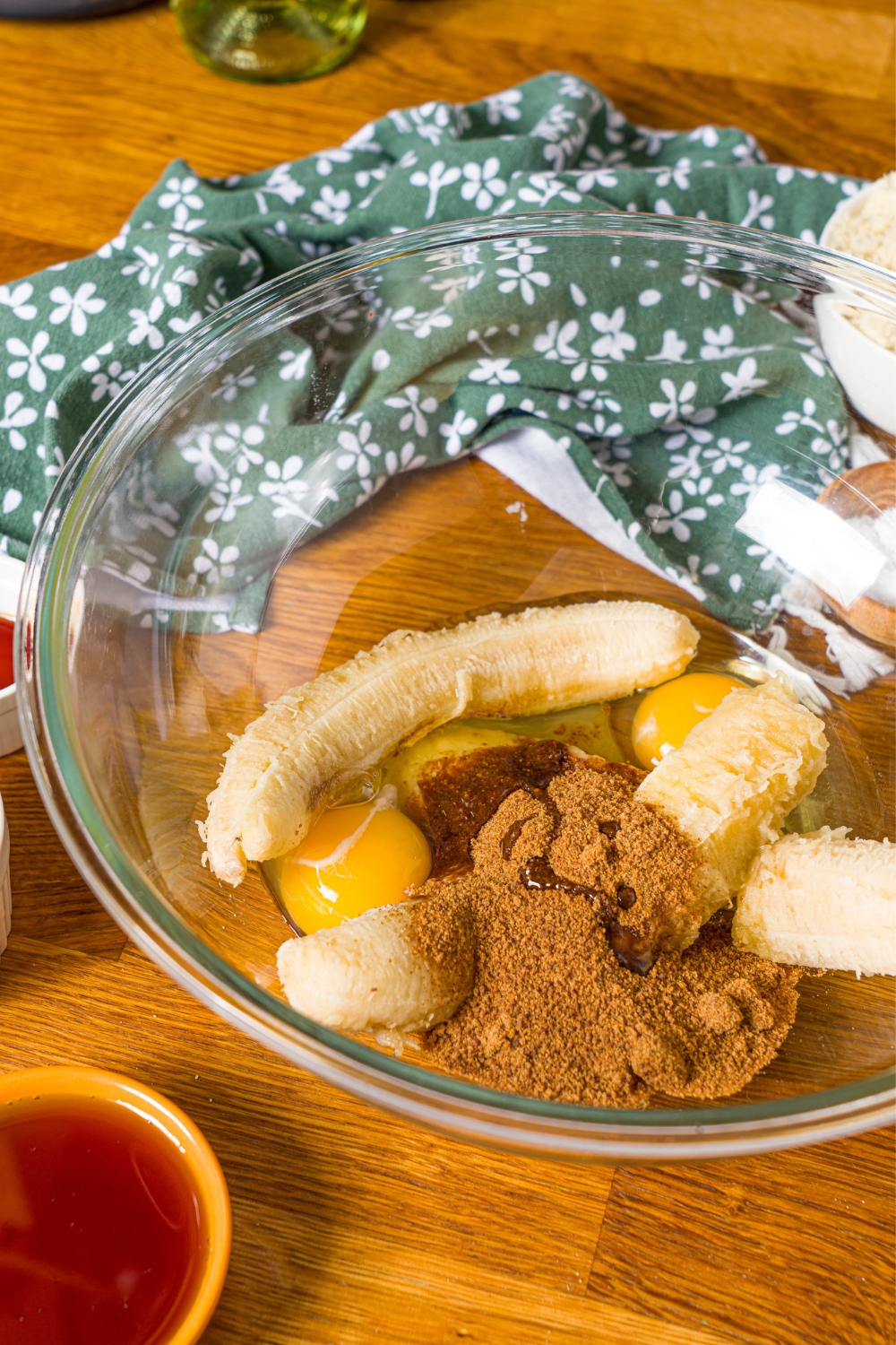 A large bowl with bananas, cinnamon, and eggs. The bowl is on a wooden counter with a green floral napkin.