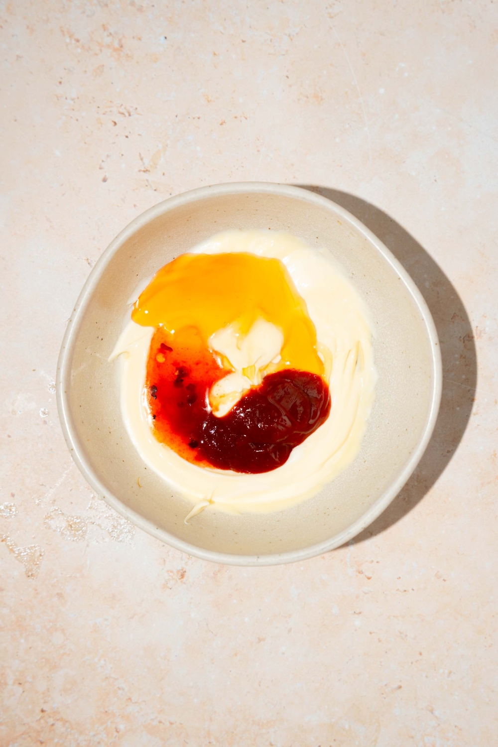 A bowl with ingredients to make bang bang sauce including mayo, honey, sweet chili sauce, and tabasco. The bowl is on a tan counter.