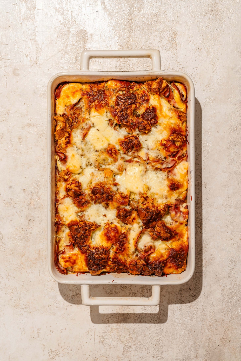 A baking dish with baked croissant breakfast casserole with ham and cheese. The dish is on a tan counter.
