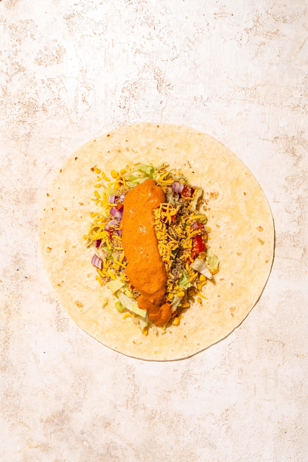 An open burrito with various toppings finished with burrito sauce. The burrito is on a tan counter.