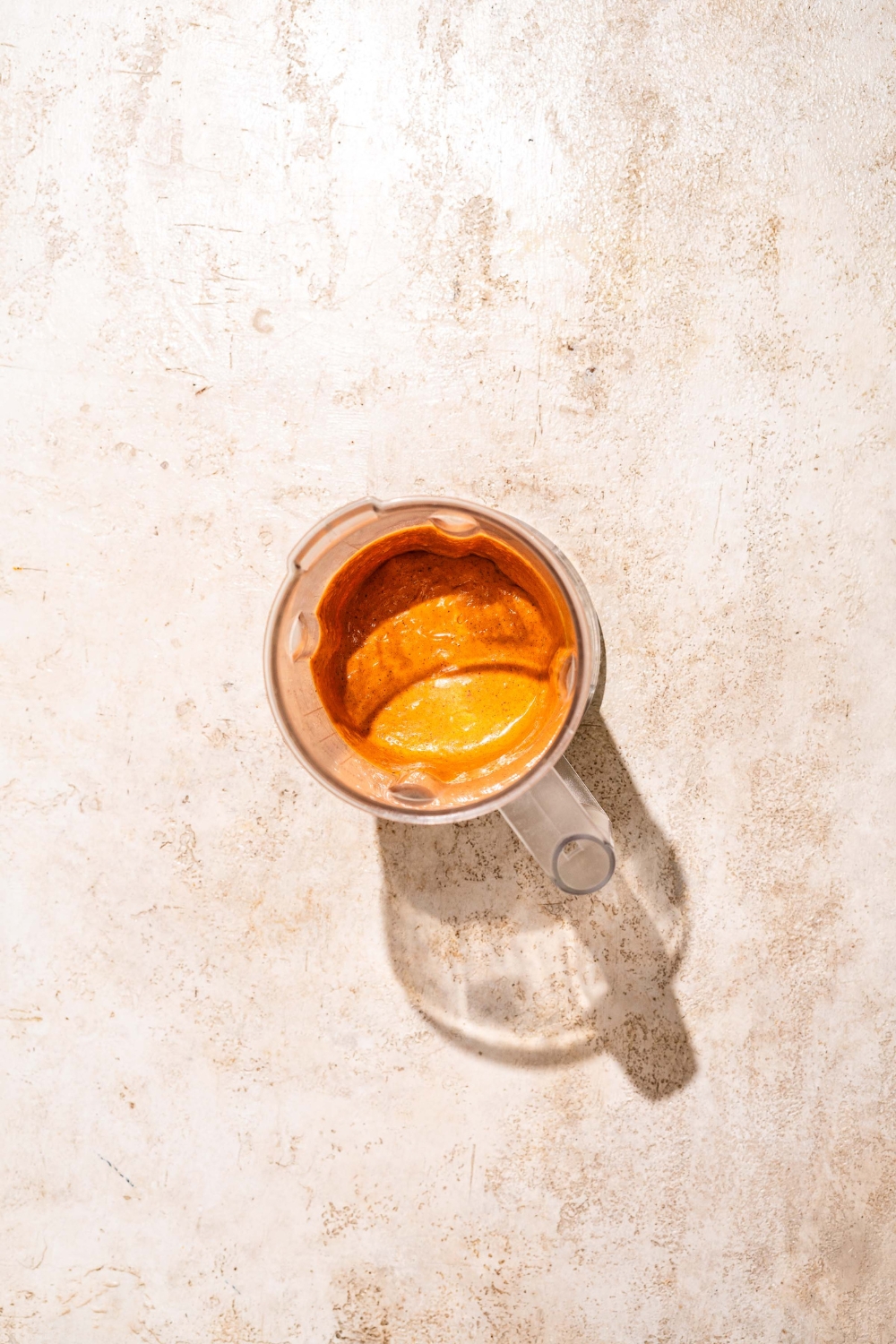 A blender jar with blended burrito sauce. The jar is on a tan counter.