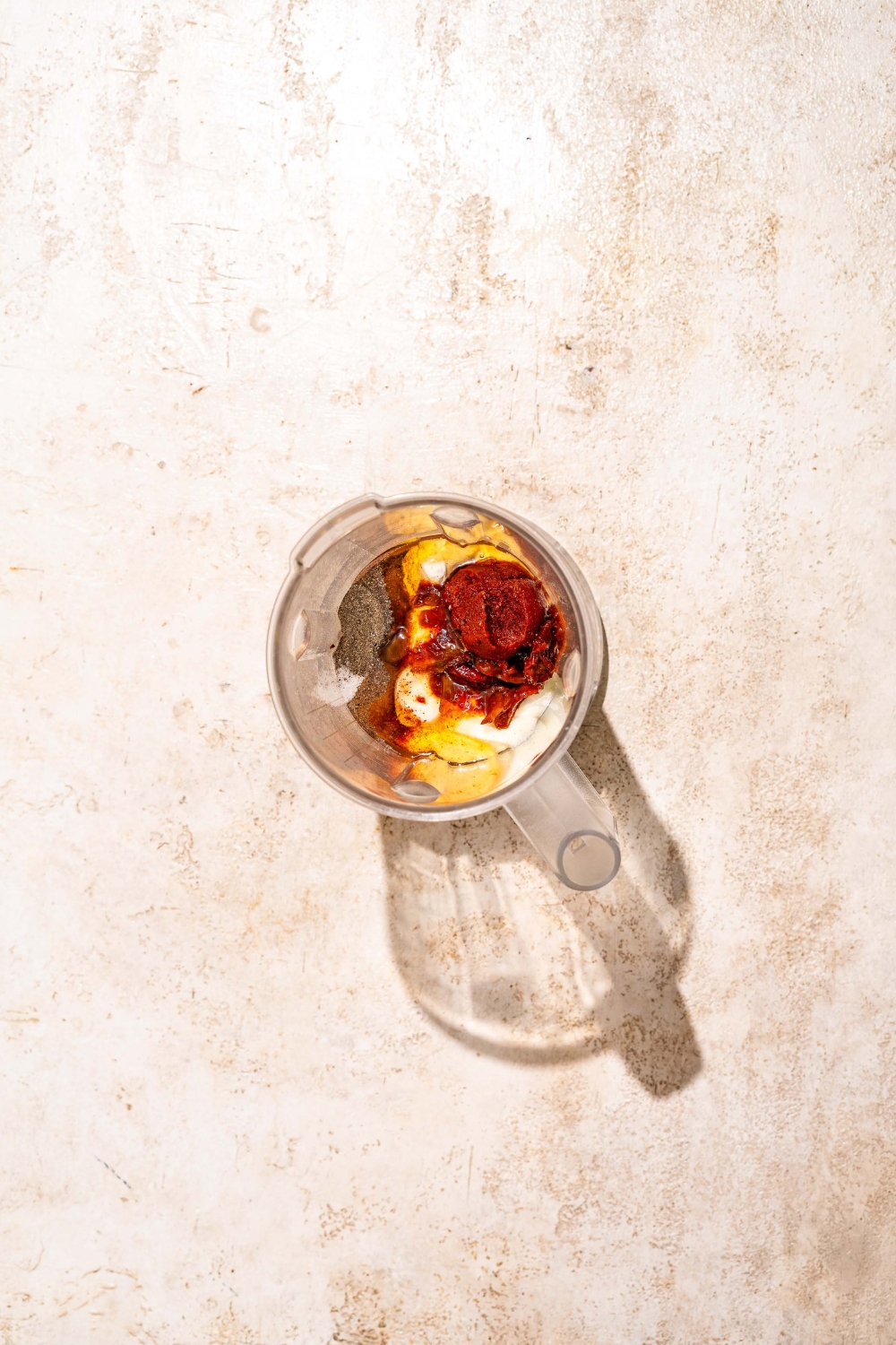 A blender with ingredients to make burrito sauce including greek yogurt, sour cream, chipotle peppers, and spices. The jar is on a tan counter.
