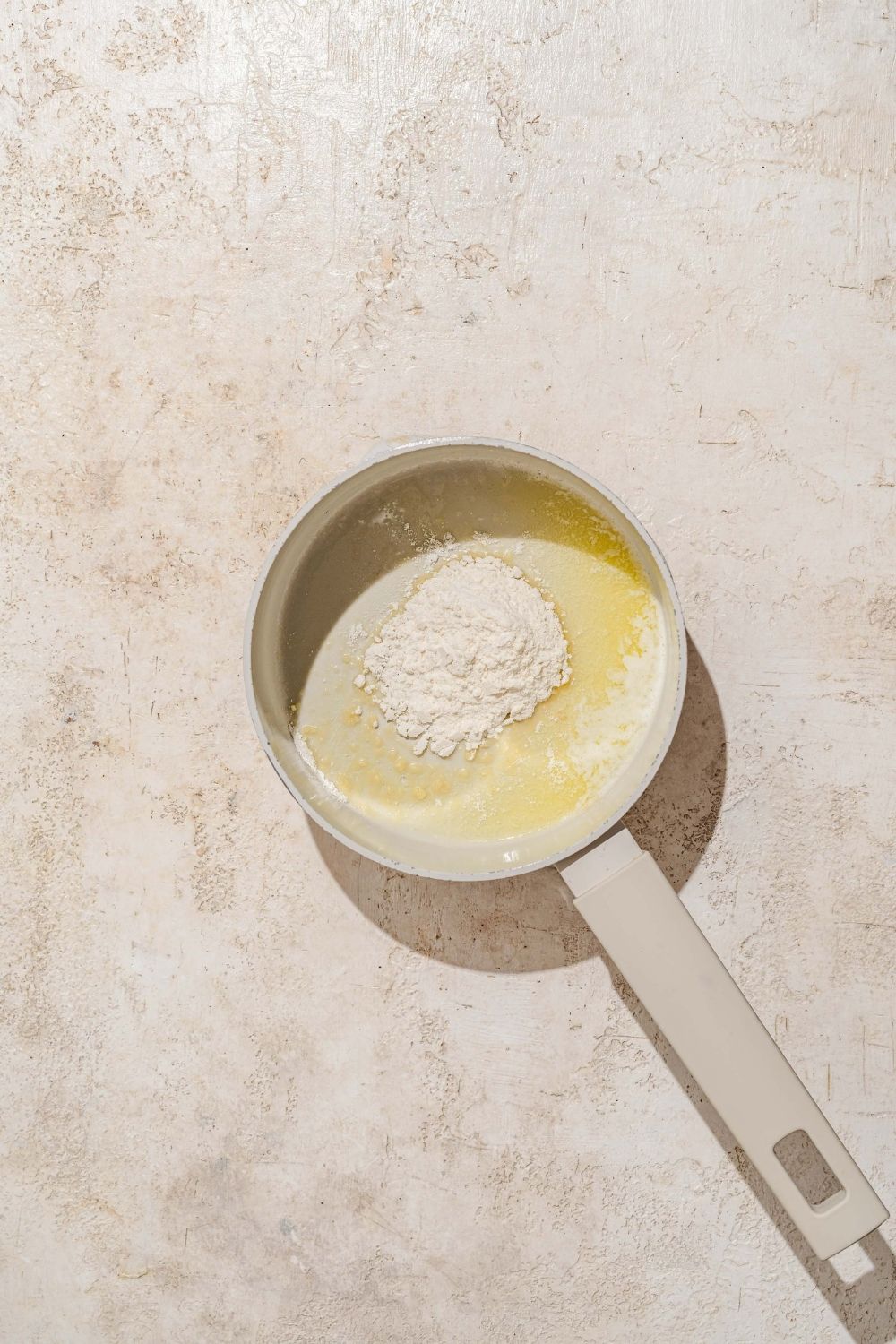 A saucepan with a flour and butter mixture to make a roux. The saucepan is on a tan counter.