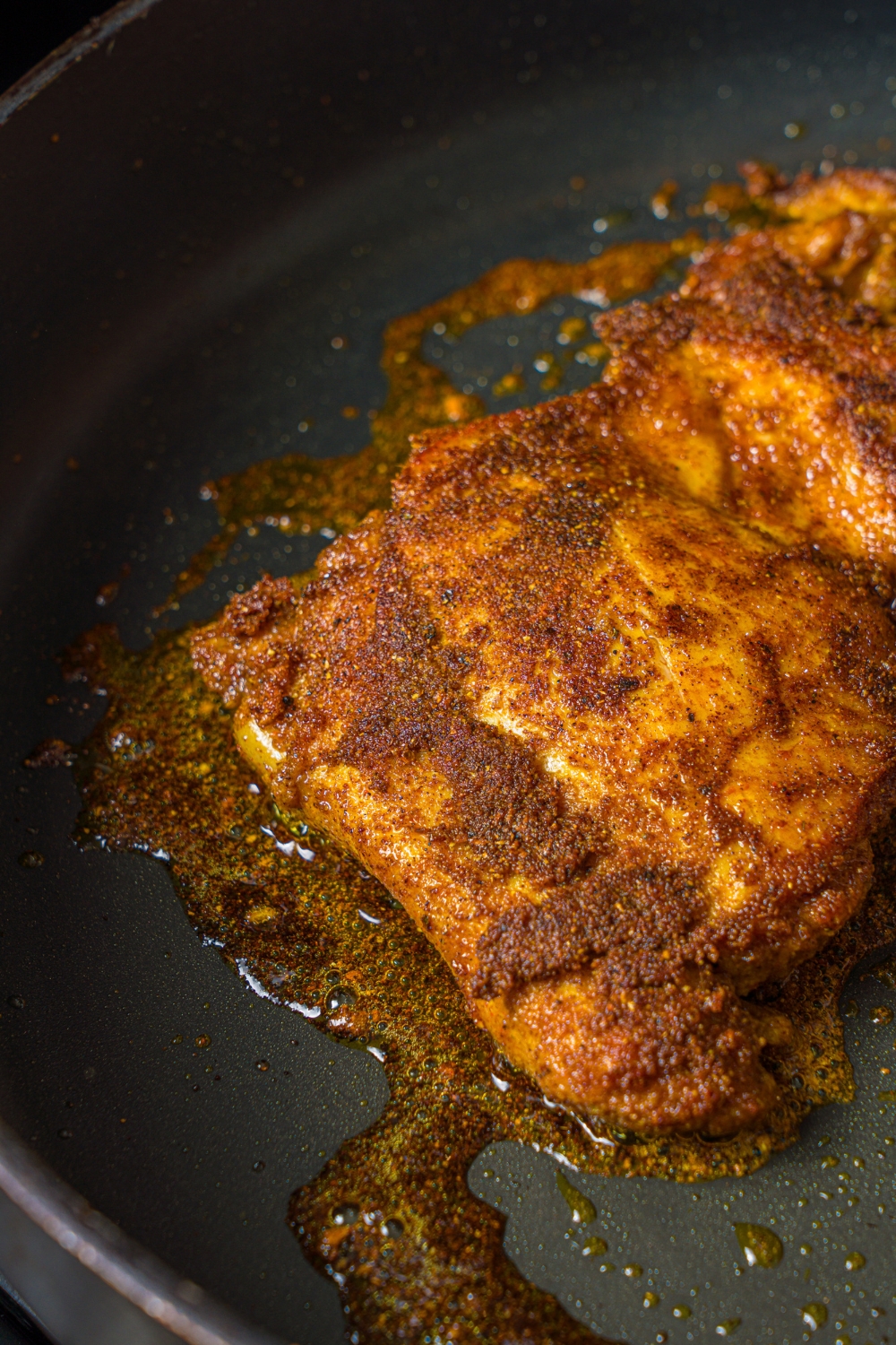 A skillet with marinated chicken cooking in oil.