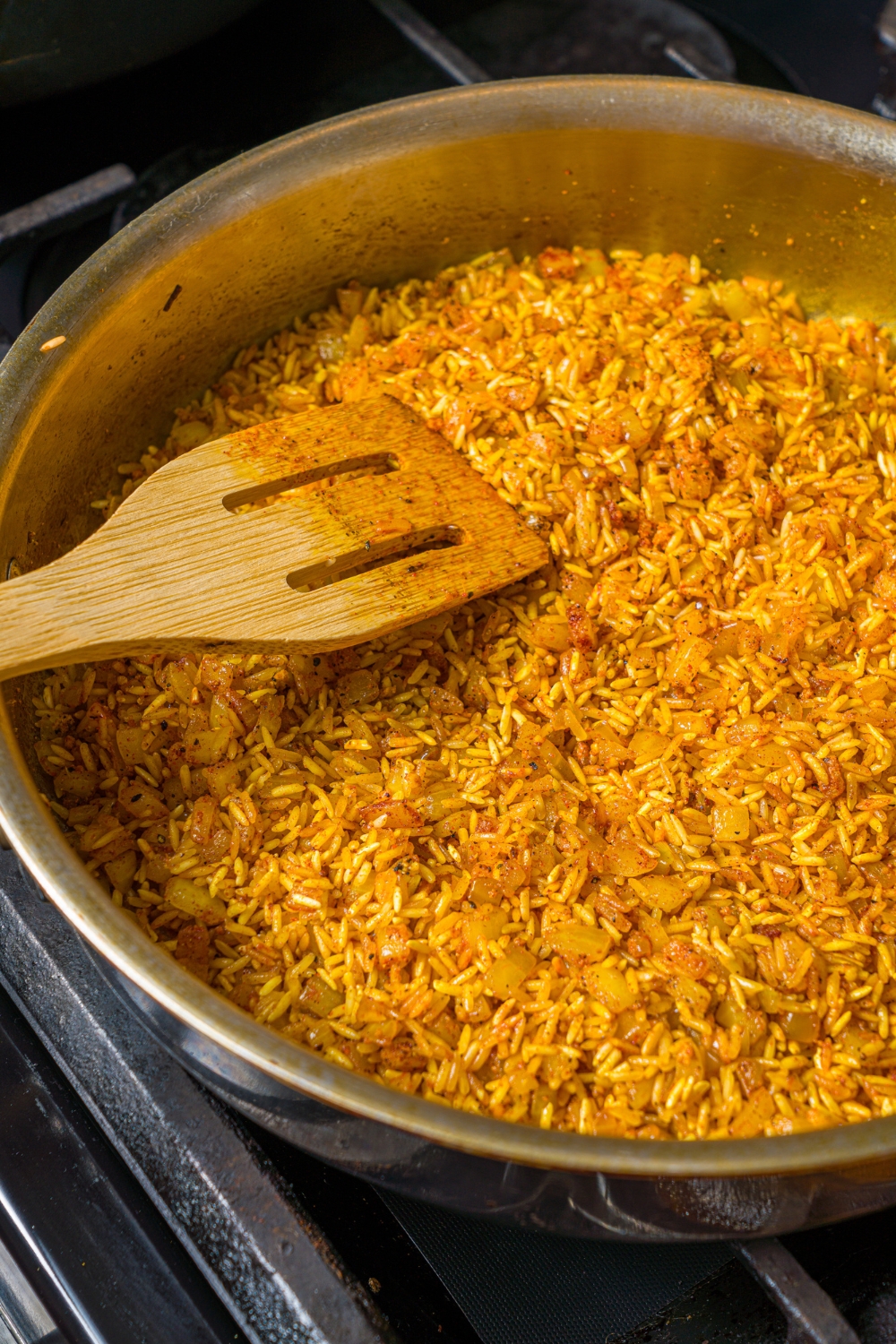 A skillet with a wooden spoon mixing cooked rice and shawarma seasonings.