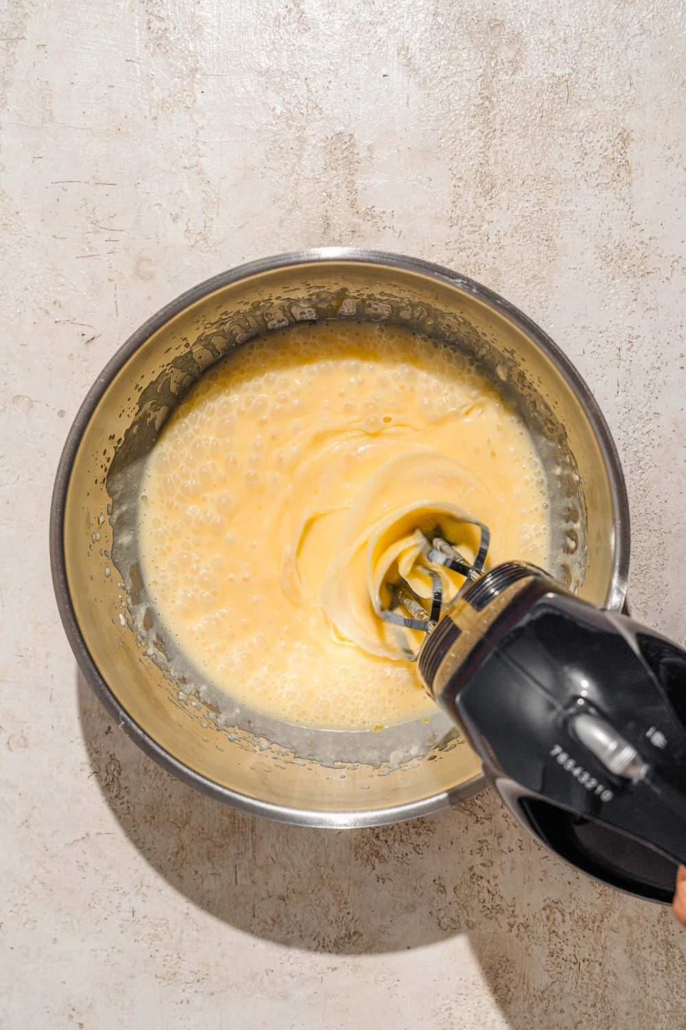 A large bowl in a kitchen stand mixer mixing wet ingredients for chocolate cake batter. The bowl is on a tan counter.