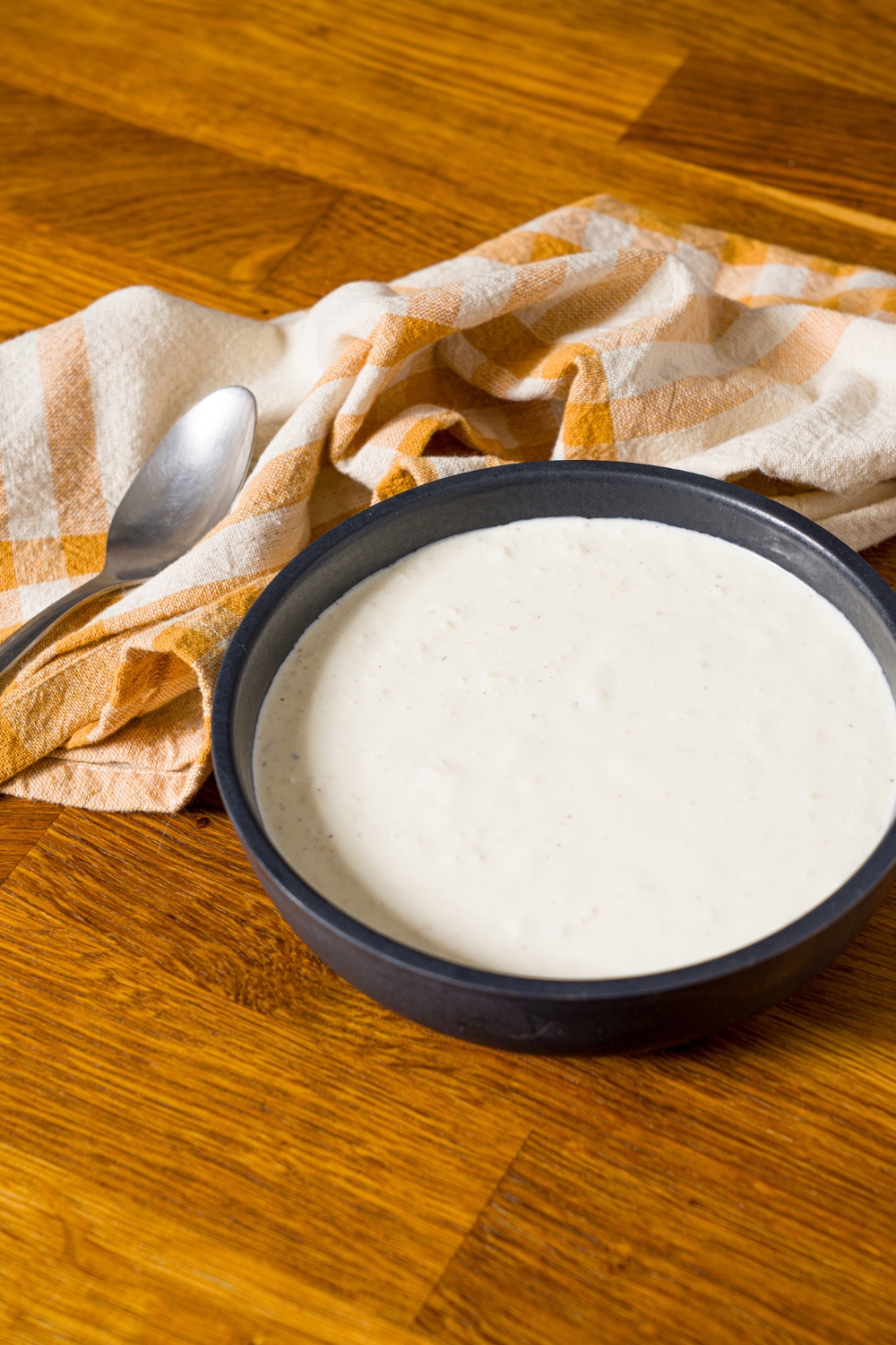A bowl of horseradish sauce on a wooden counter with a yellow checkered napkin.