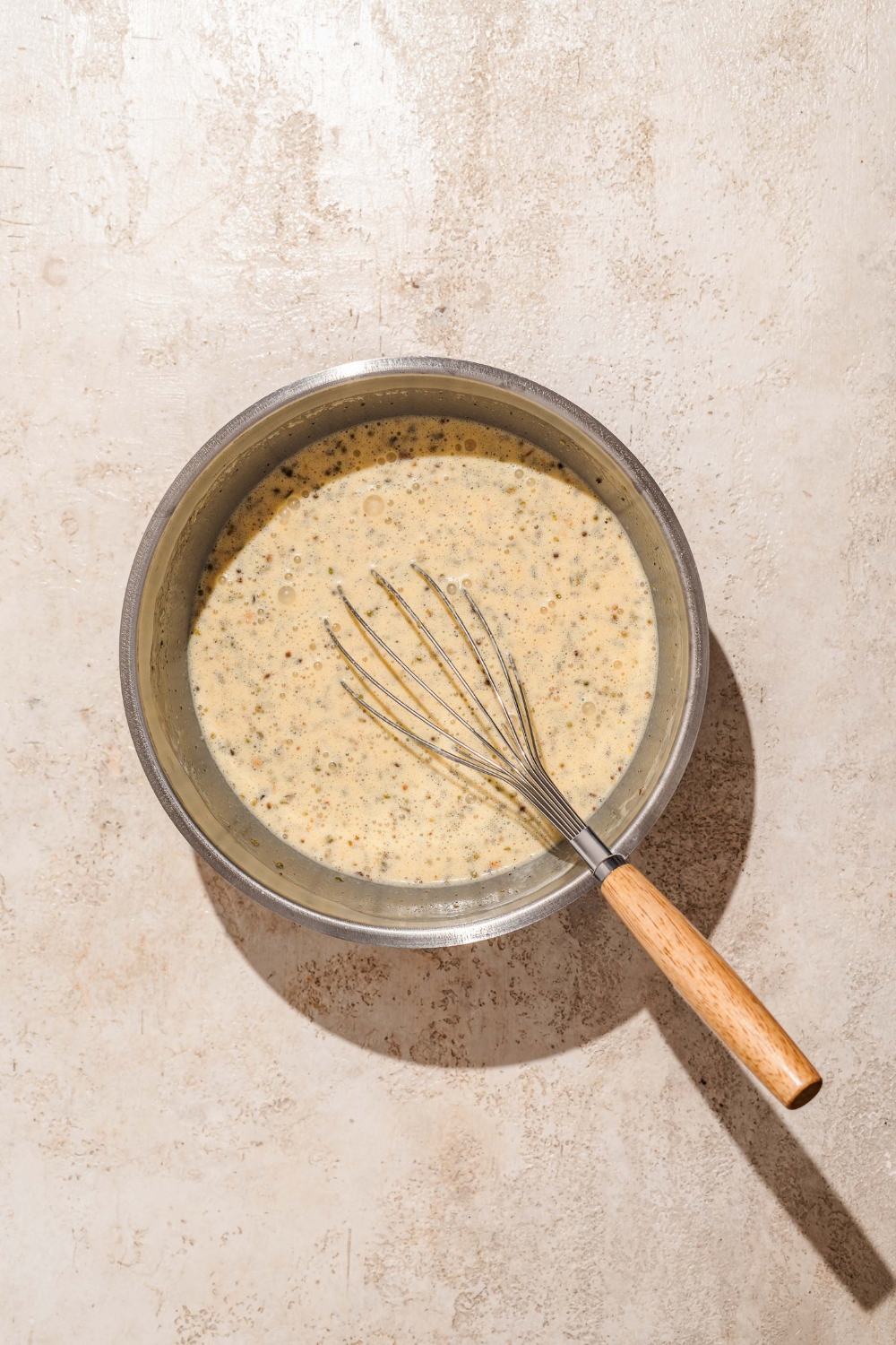 A large bowl with a whisk mixing a custard for croissant breakfast casserole. The bowl is on a tan counter.