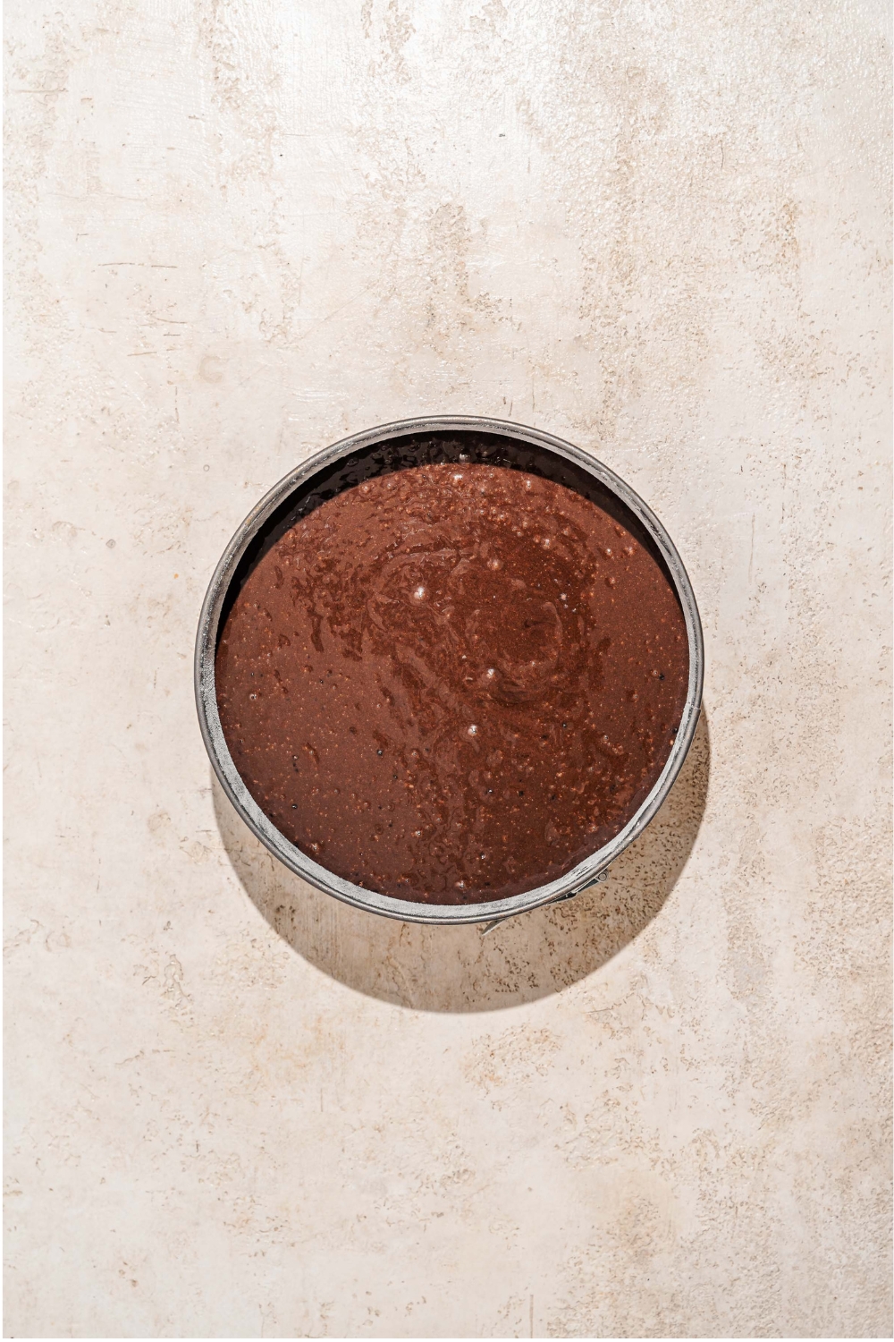 A cake tin with chocolate cake batter. The tin is on a tan counter.