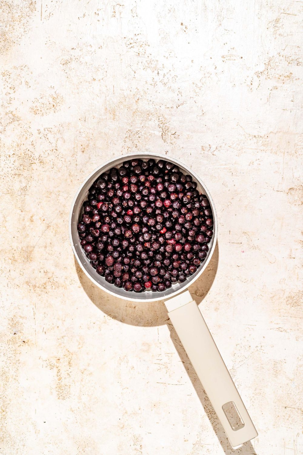 A saucepan with frozen elderberries. The pot is on a tan counter.