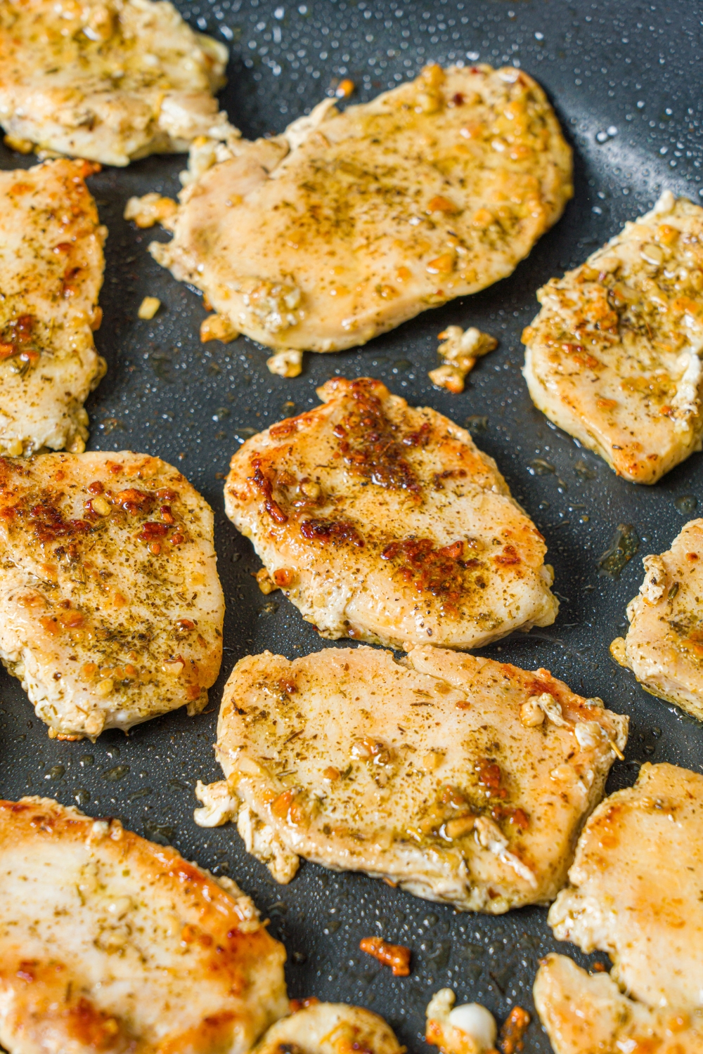 A skillet with sliced seasoned chicken searing in oil.