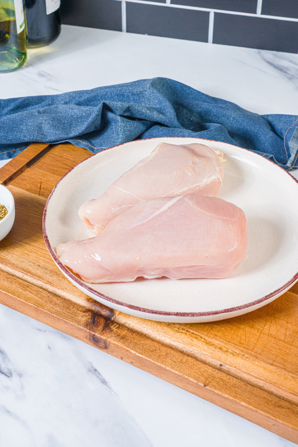 A white plate with defrosted chicken breasts. The plate is on a wooden board with a blue cloth napkin.
